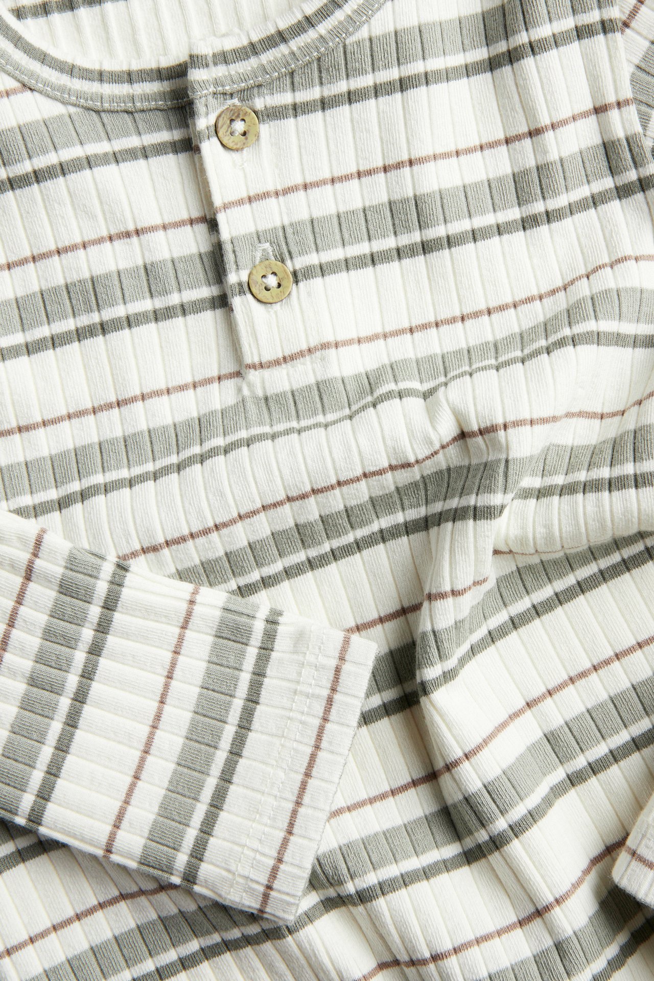 Close-up of a baby's ribbed long-sleeved off-white bodysuit with greenish-gray and brown stripes, featuring two front buttons.