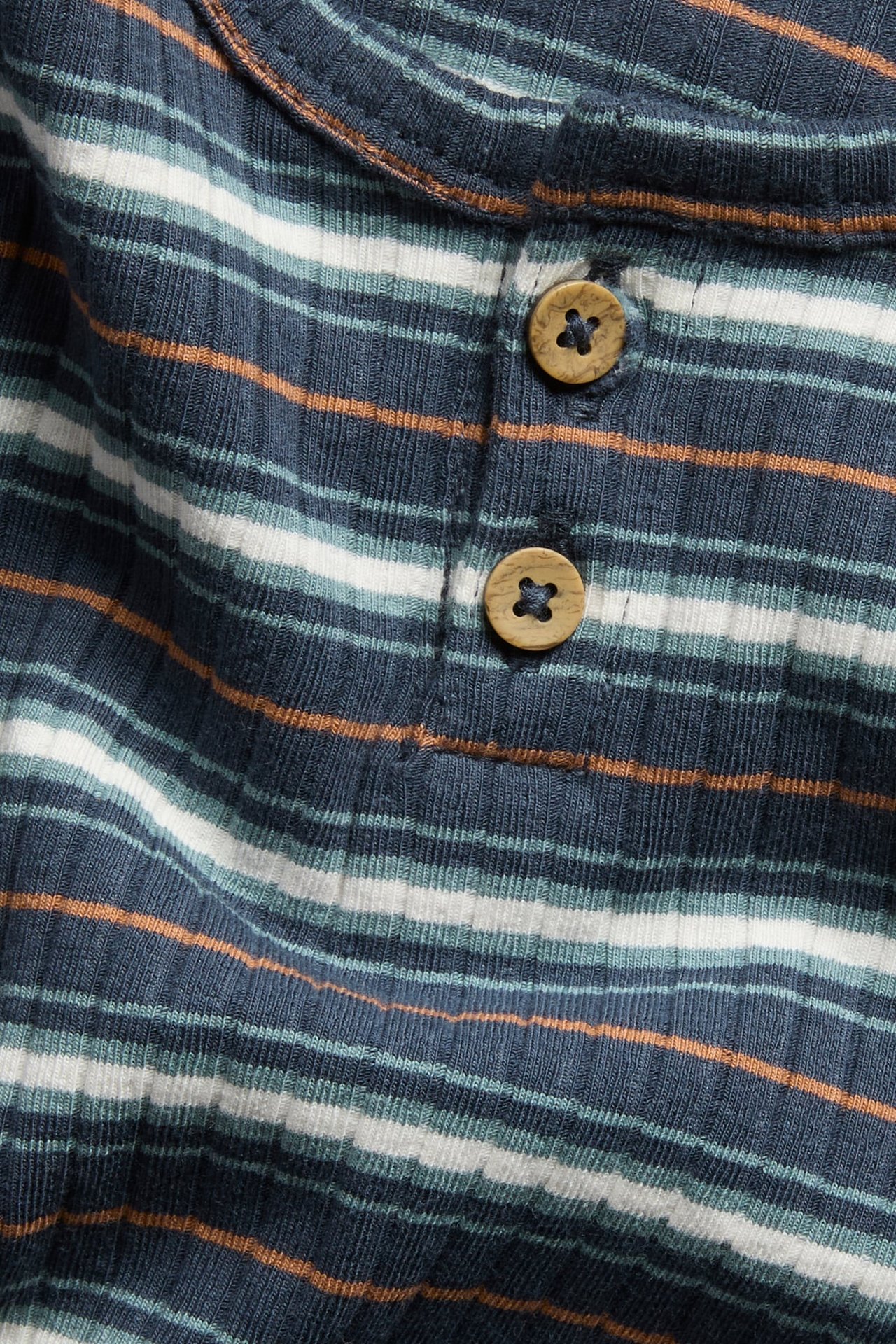Nahaufnahme: gestreiftes Rippshirt in Marineblau, Weiß und Orange, mit zwei Holzknöpfen.