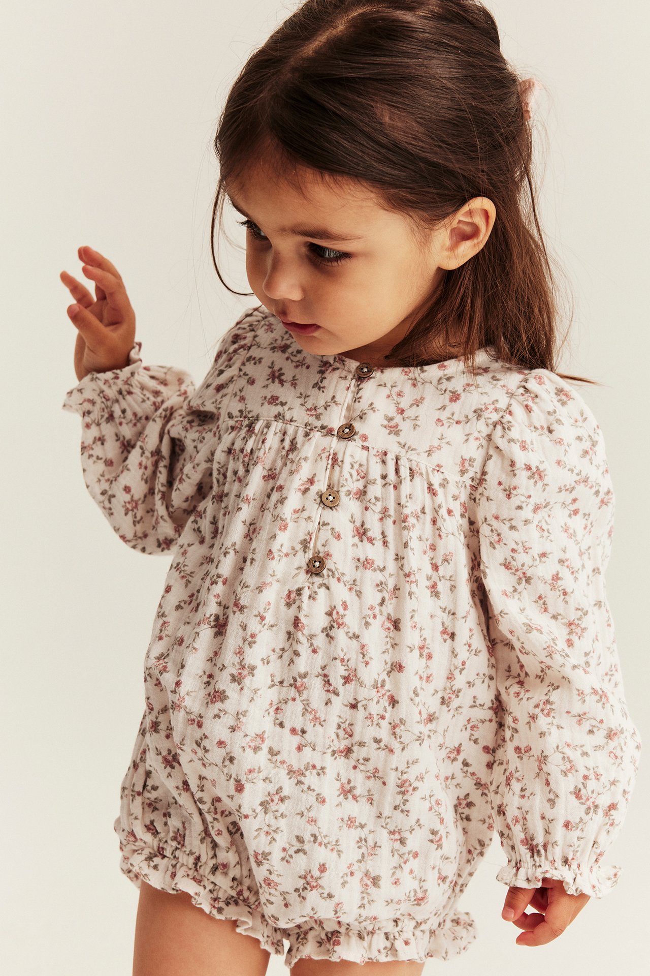 Close-up of a kid girl in an offwhite small floral muslin long-sleeved bodysuit with front buttons.