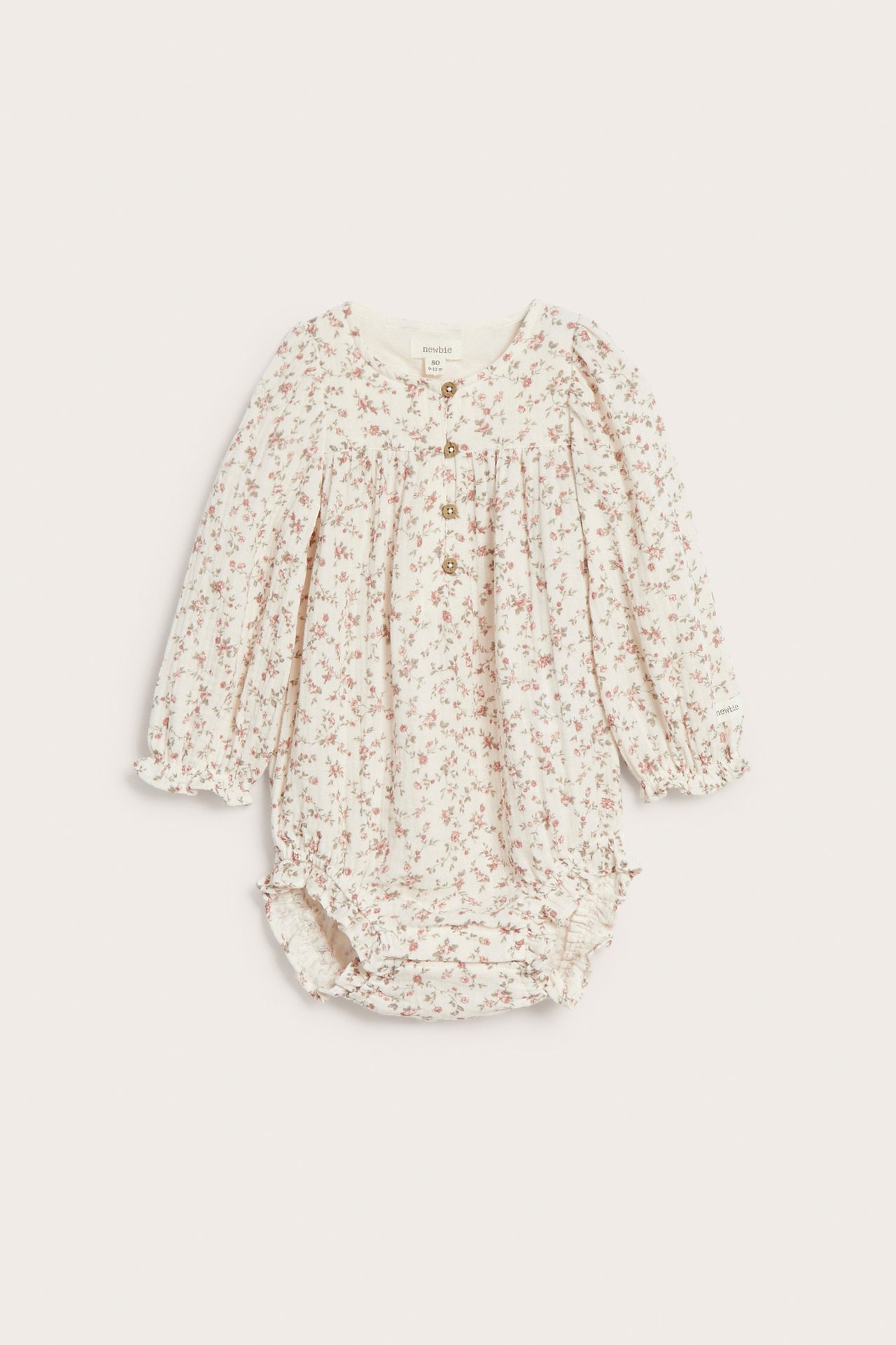 Vorderansicht eines off-white Baby Langarm-Muslinbodys mit kleinem Blumenmuster, elastischen Bündchen und Knöpfen vorne.