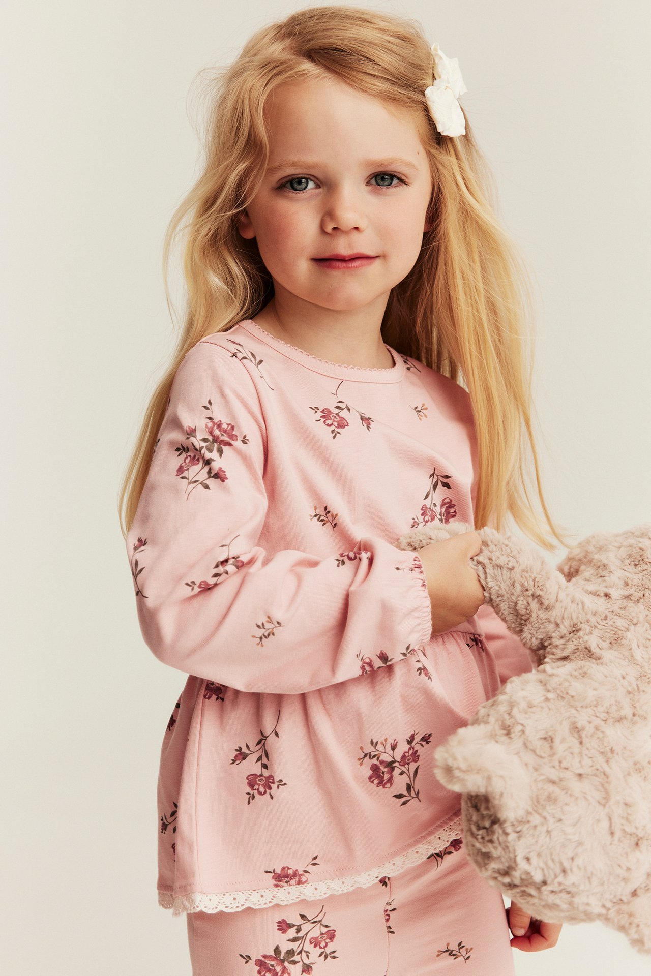 Front view, kid in a pink floral peplum top with lace hem and picot neckline, holding a teddy.