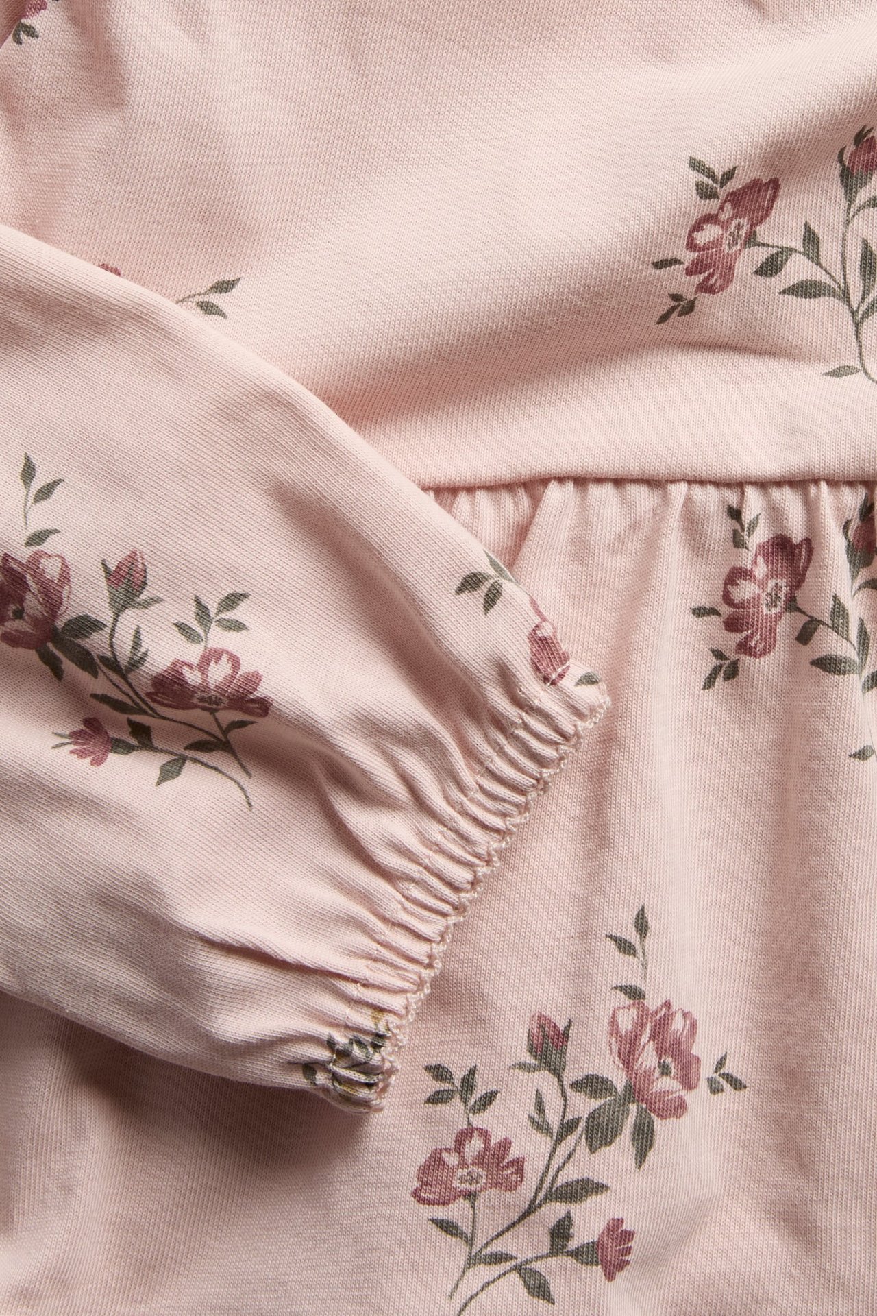 Nahaufnahme: hellrosa, geblümtes Baumwoll-Peplum-Top mit geraffter Taille und elastischen Ärmeln.
