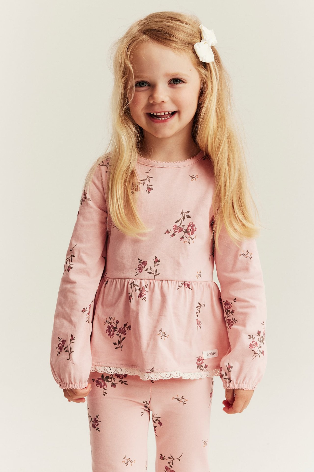 Front view of a smiling kid wearing a light pink floral peplum top with lace trim and matching leggings.