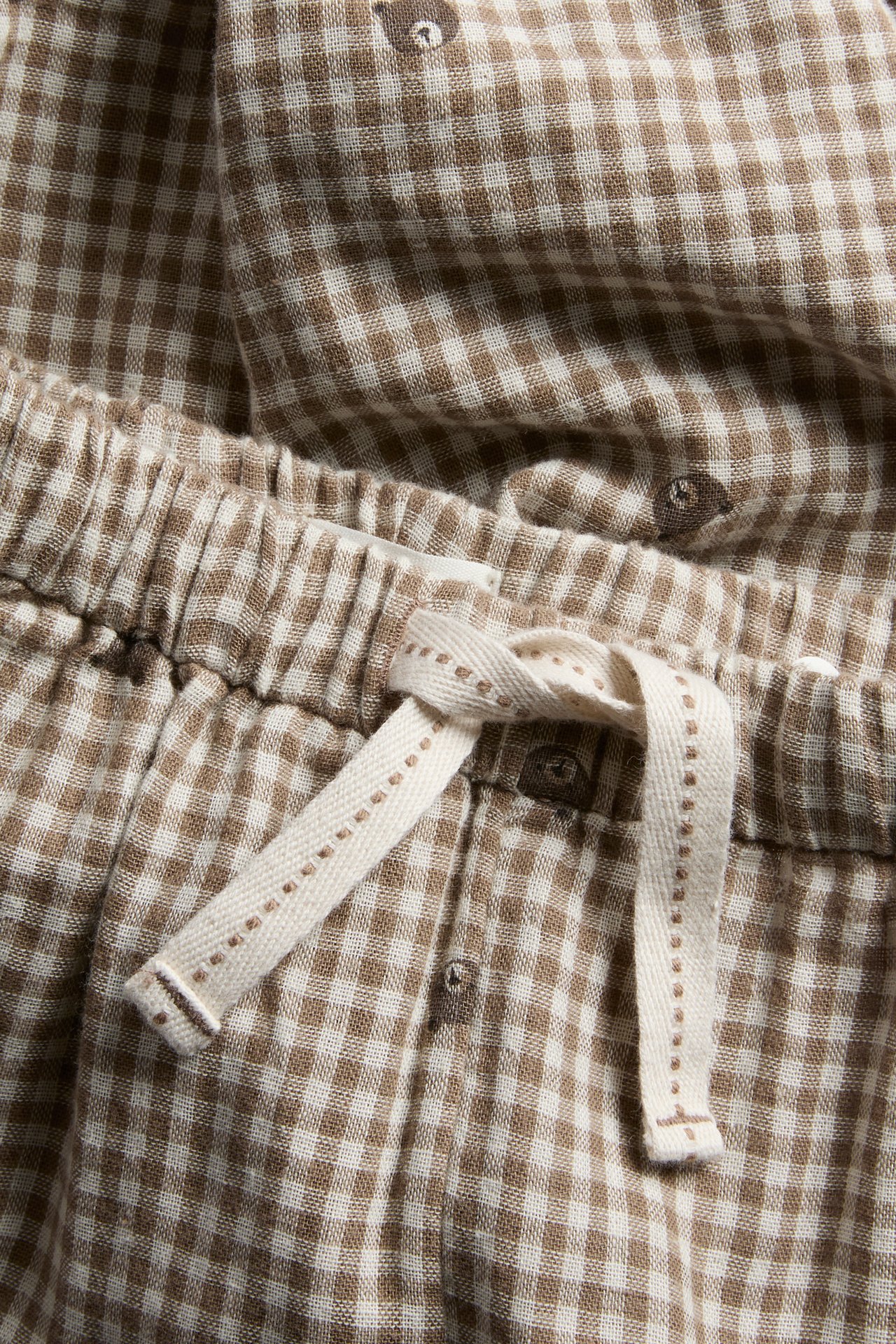 Nahaufnahme von braun-weißer Gingham-Pyjamahose mit Bärenmuster und Kordelzug am Bund.