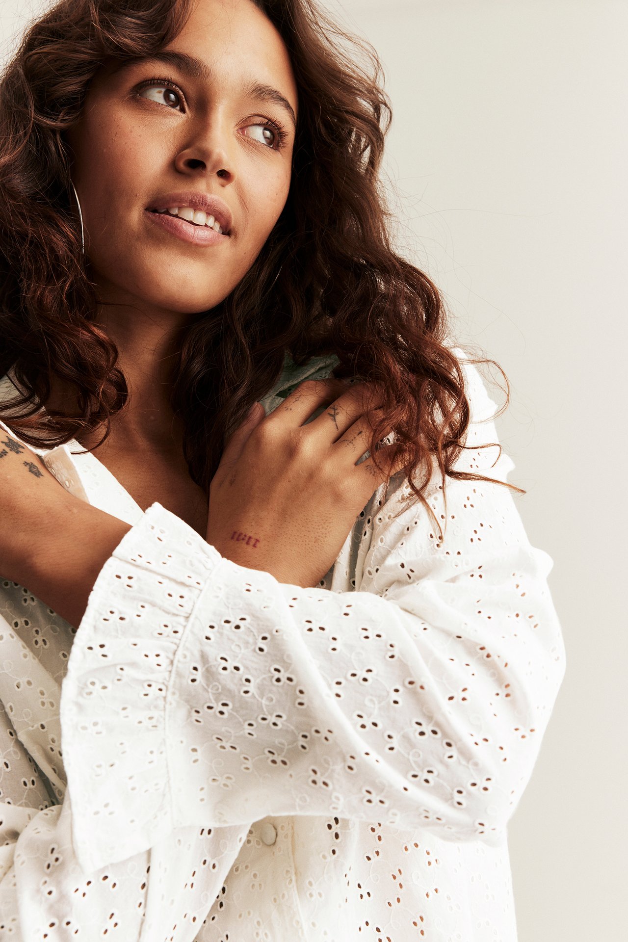 Close-up of a woman in an off-white broderie anglaise pyjama top with ruffled cuffs and covered buttons.