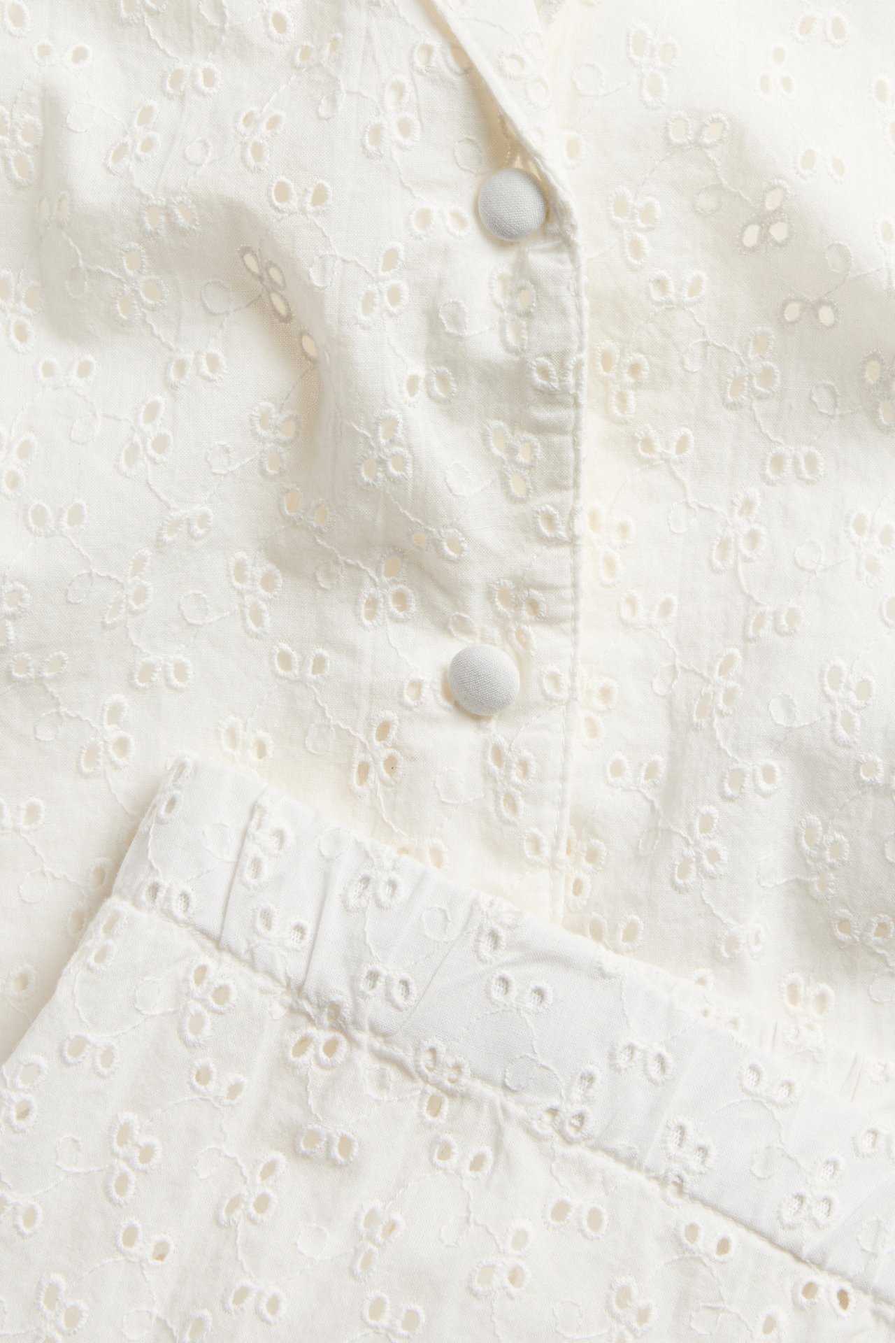 Close-up of off-white cotton pyjama set with broderie anglaise, covered buttons, and elastic waistband.