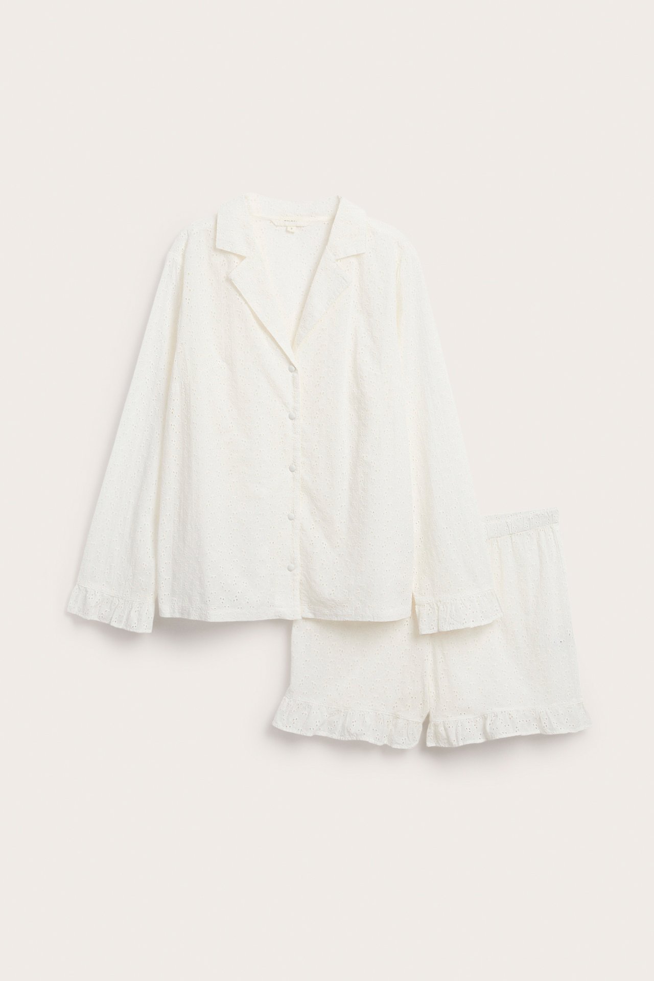 Front view: Off-white cotton broderie anglaise pyjama set, long-sleeved shirt and shorts with ruffle details.