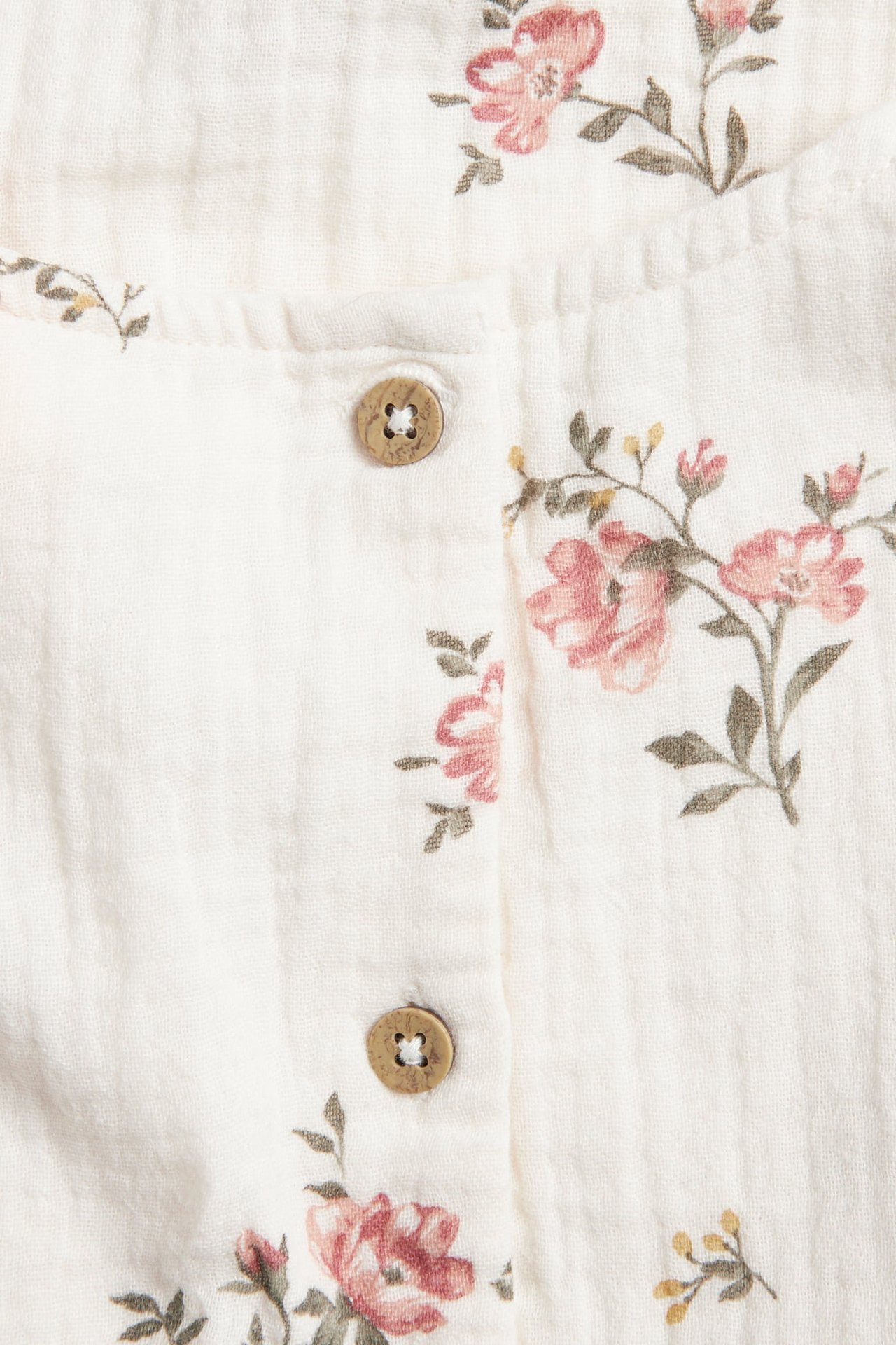 Close-up view of an off-white floral muslin dress with a pink floral pattern and two wooden buttons.