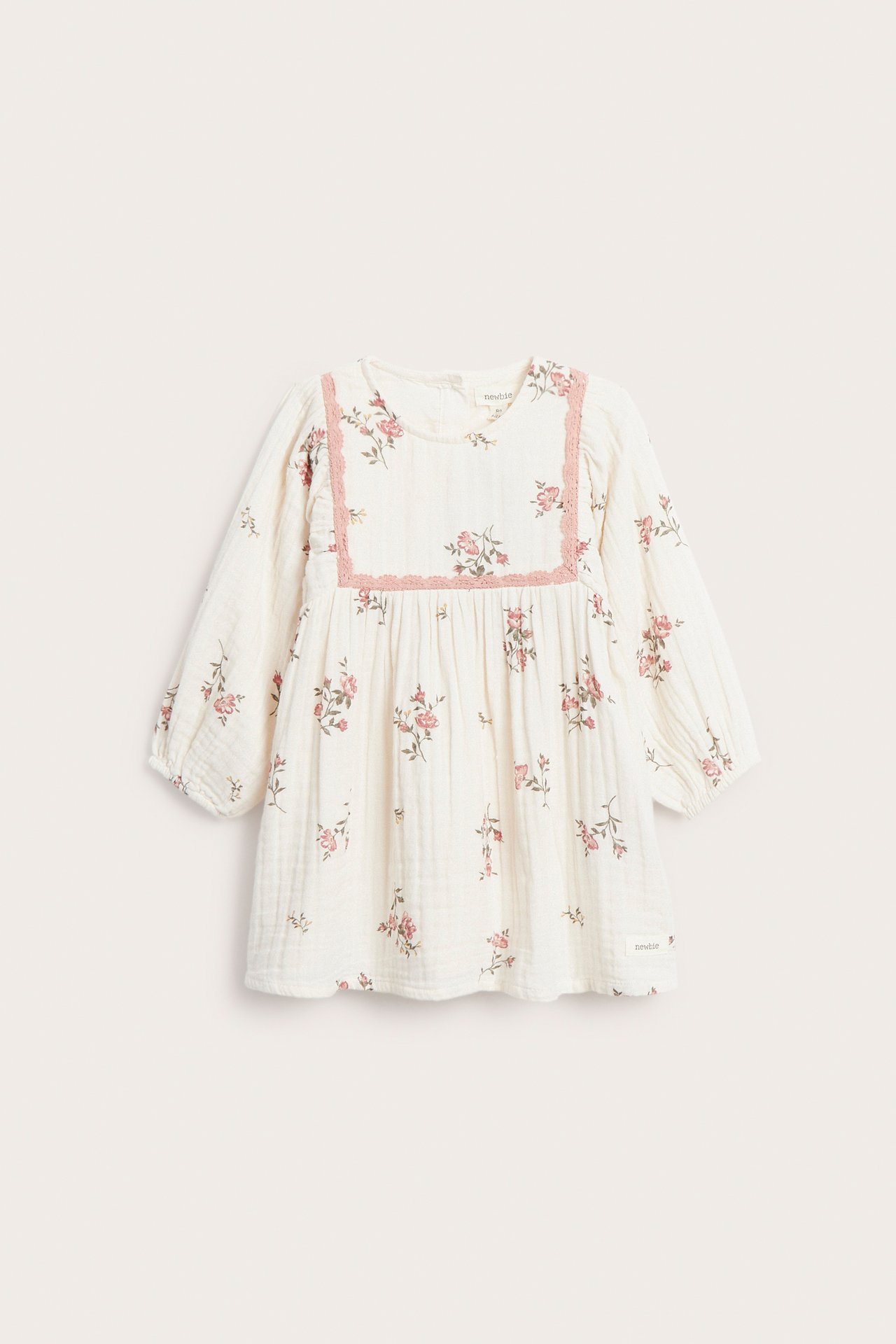 Front view of an offwhite muslin baby dress with pink floral print and pink lace trim.