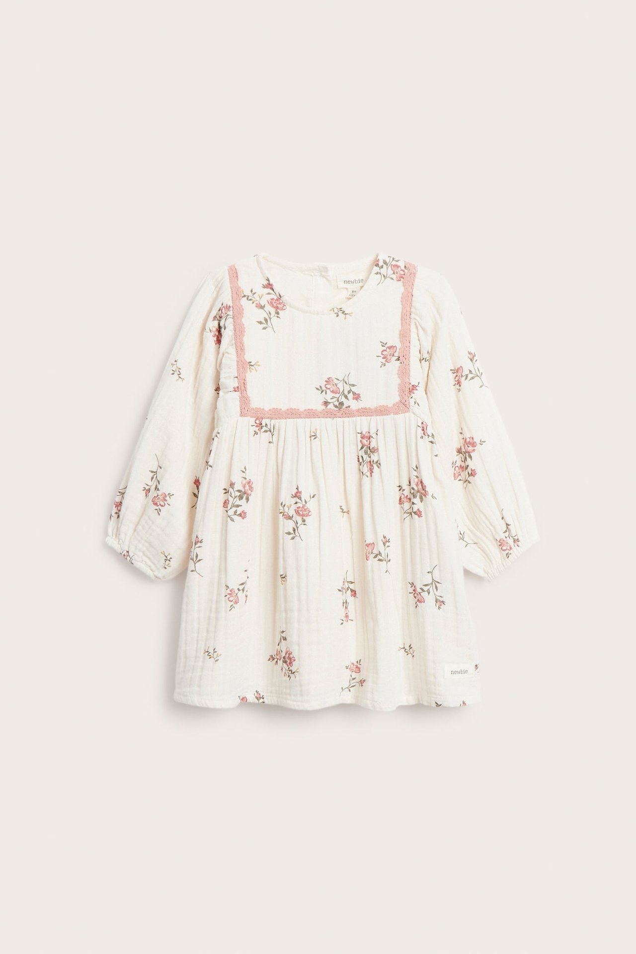 Vorderansicht eines cremeweißen Musselin-Babykleides mit rosa Blumenmuster und rosa Spitzenbesatz.
