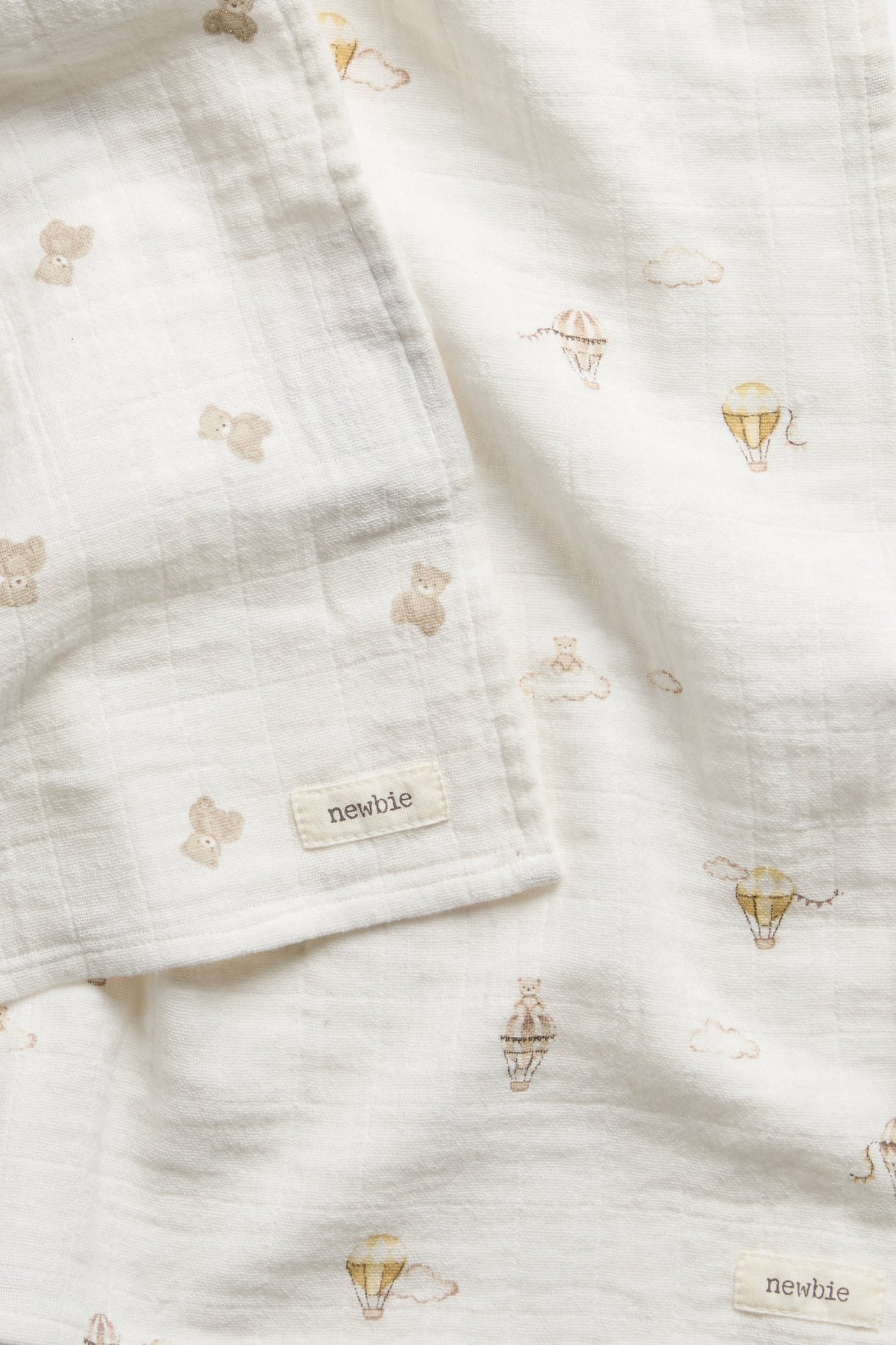 Nahaufnahme einer weißen Musselin Babydecke mit Bärchen- und Heißluftballon-Print.