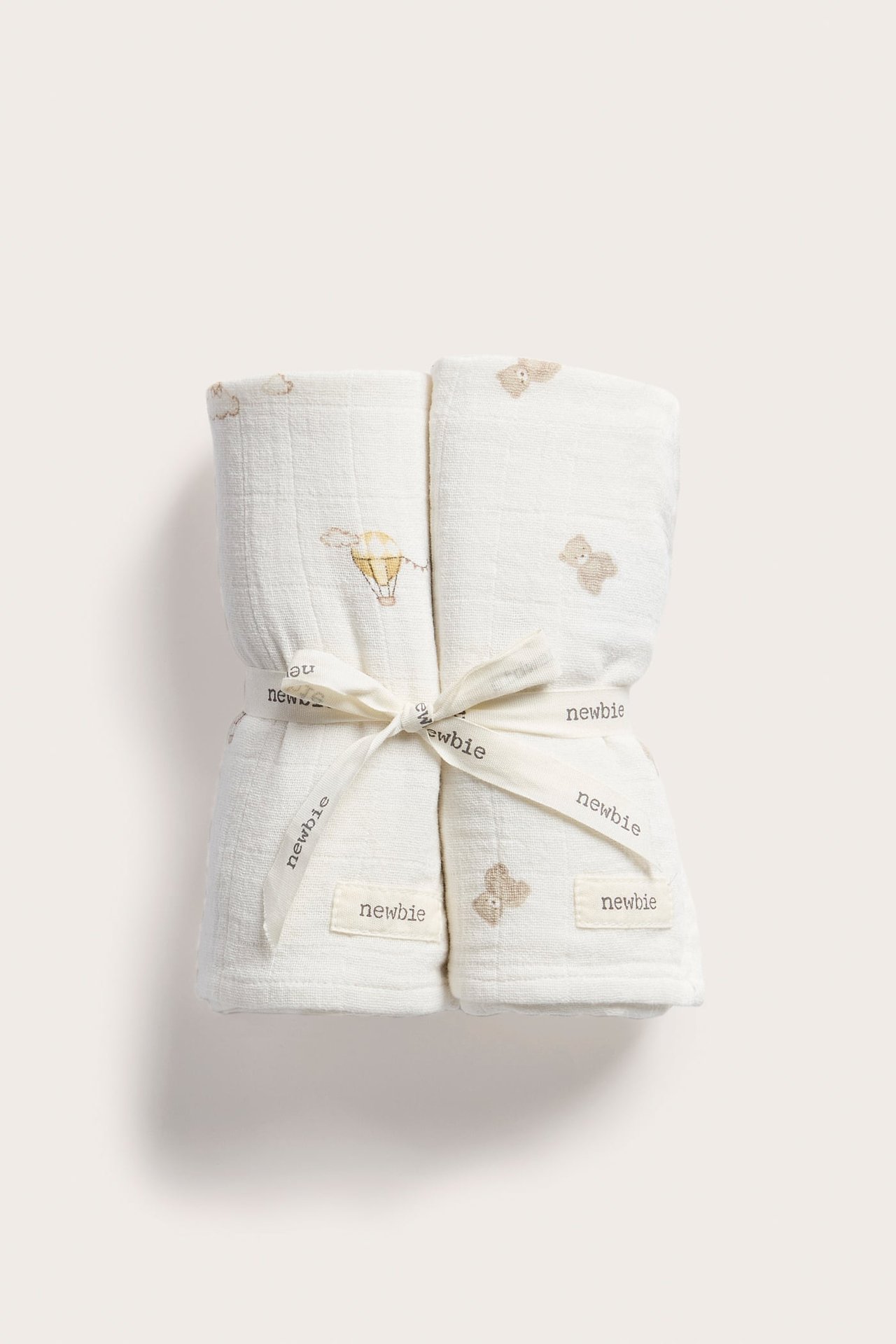 Front view of two white baby muslin blankets with hot air balloon and bear prints, tied with a ribbon.