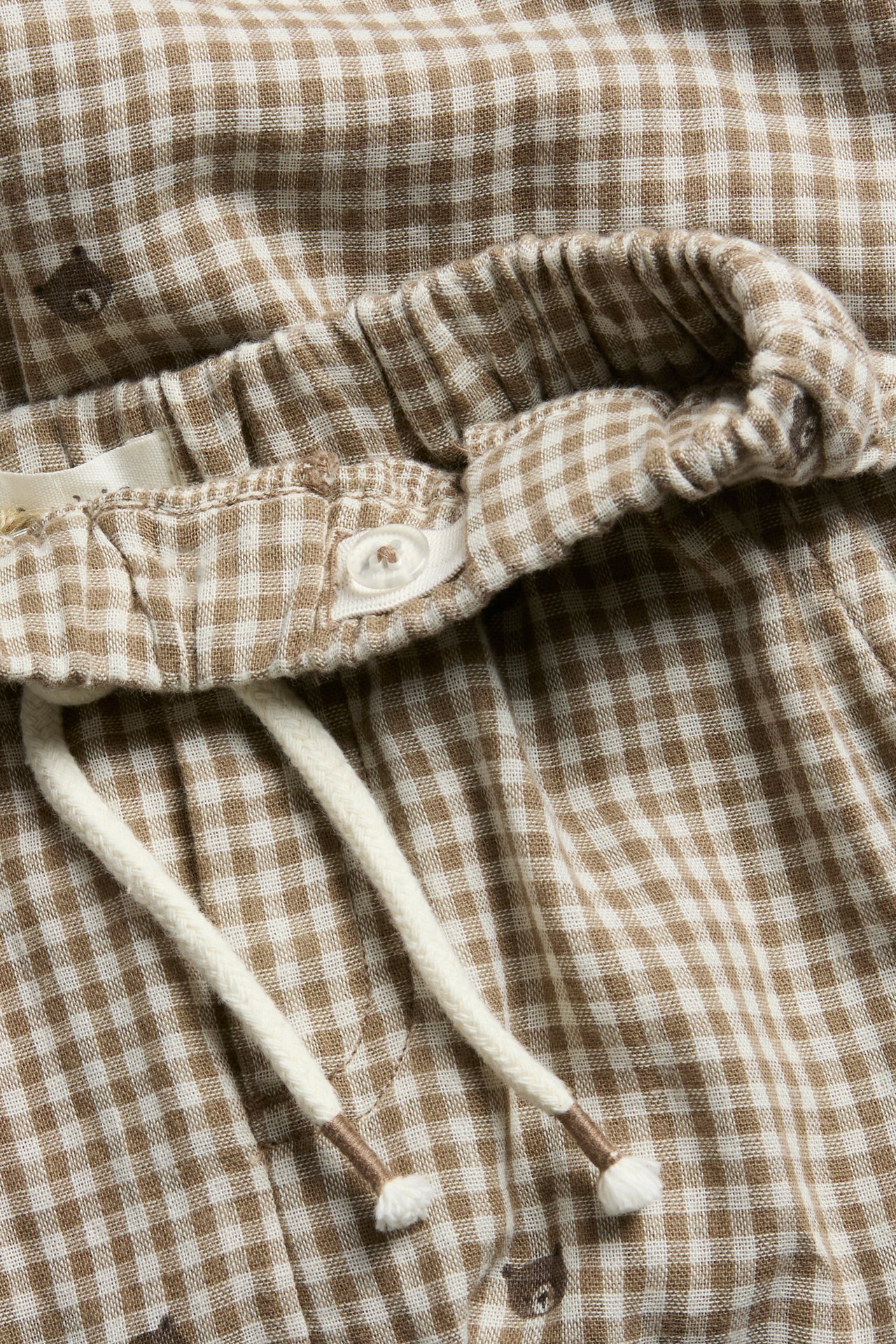 Nahaufnahme von braun-weißen Vichy-Shorts mit Gummizug, Knopf, Kordelzug und Bärendruck.