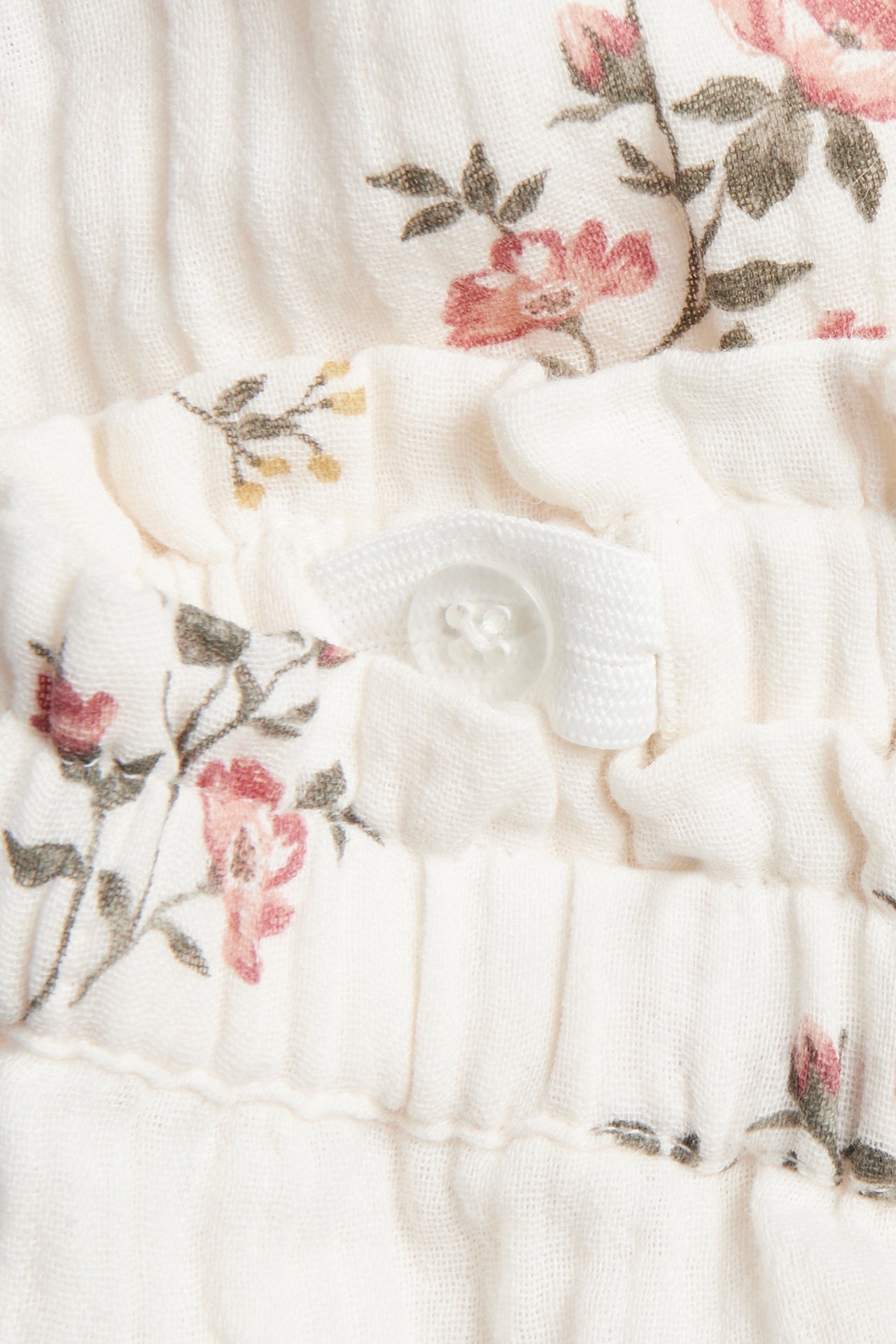 Nahaufnahme von cremeweißen geblümten gewebten Hosen mit verstellbarem Gummibund und Knopf.