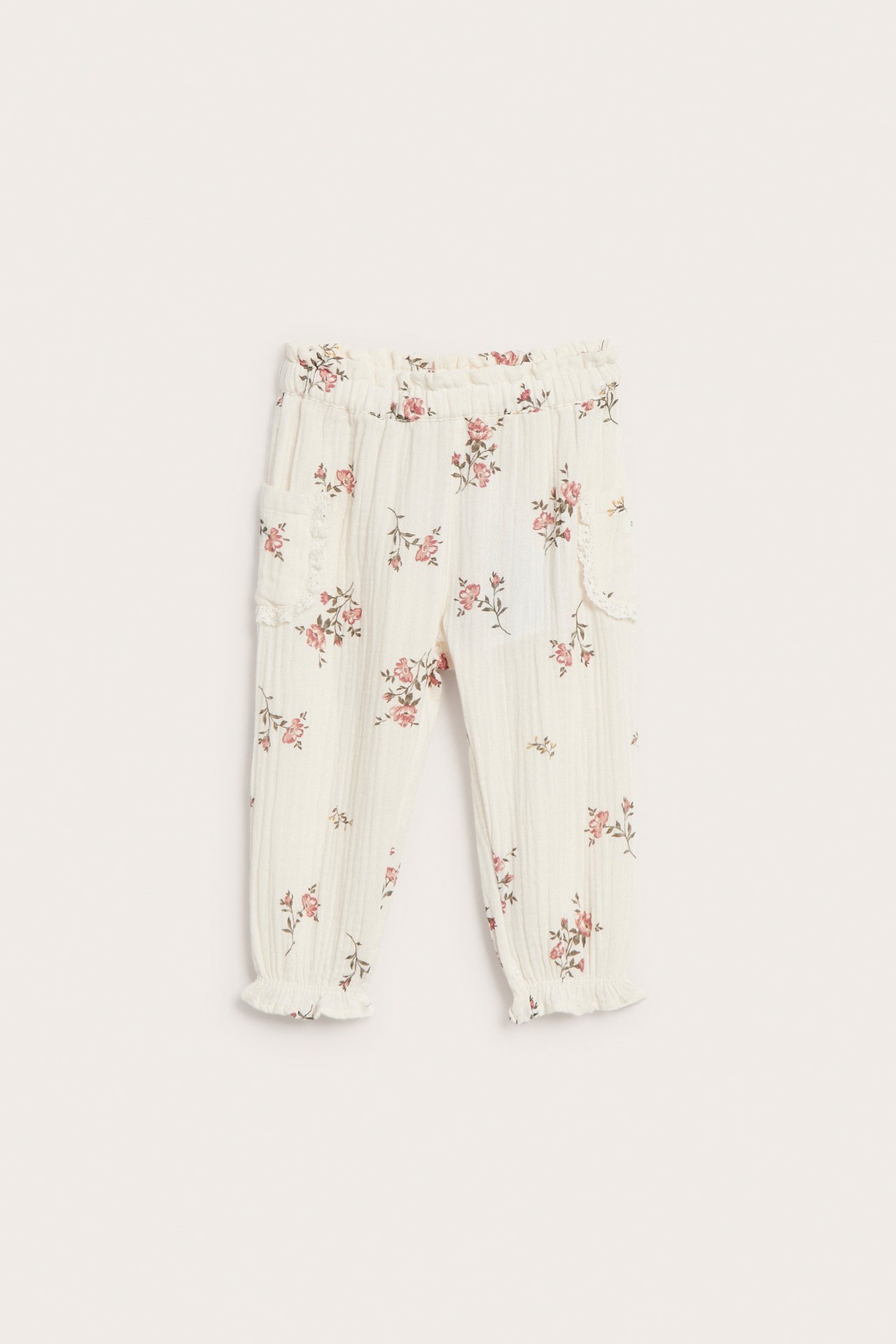 Front view of off-white floral woven pants with lace-trimmed side pockets, elastic cuffs and waist.