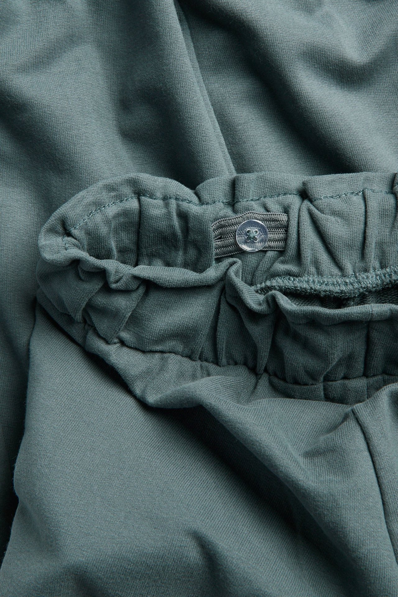 Nahaufnahme von kinder mattgrünen Hosen mit verstellbarem Gummibund und transparentem Knopf.