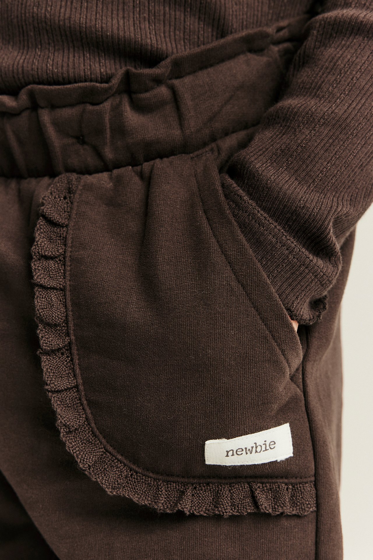 Close-up of dark brown sweatpants with ruffled pocket and a matching ribbed top on a baby.