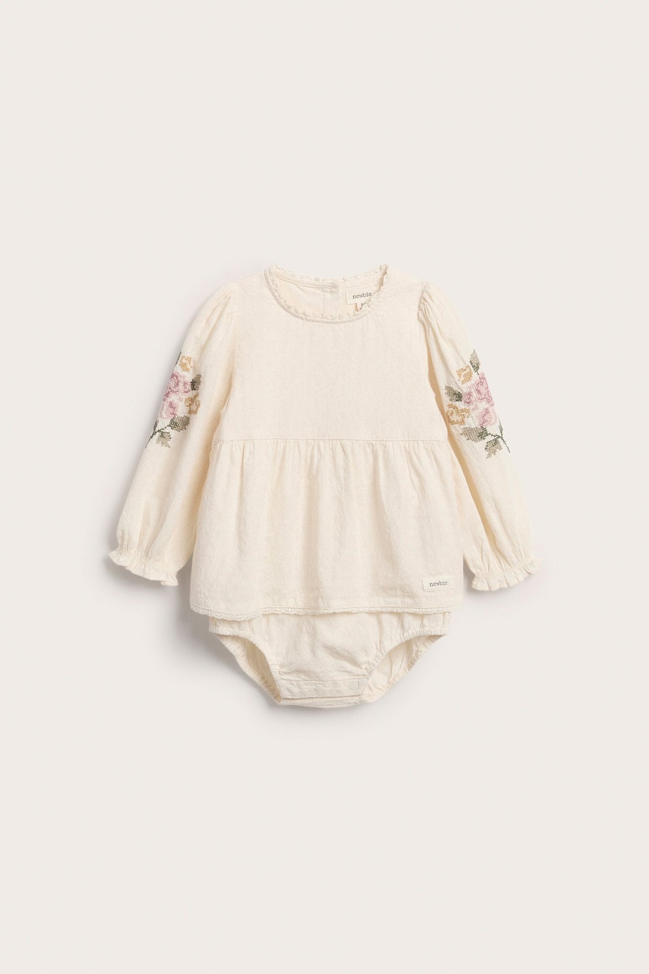 Cremeweißer gewebter Baumwoll-Babybody, Peplum-Blusenstil, mit floral bestickten langen Ärmeln.