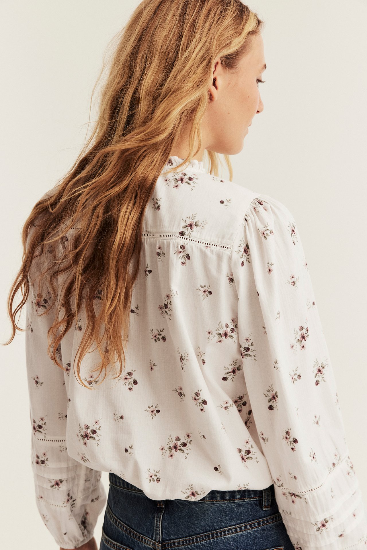 Rückenansicht: Frau in weißer floraler Bluse mit Rüschenkragen und blauer Jeans.