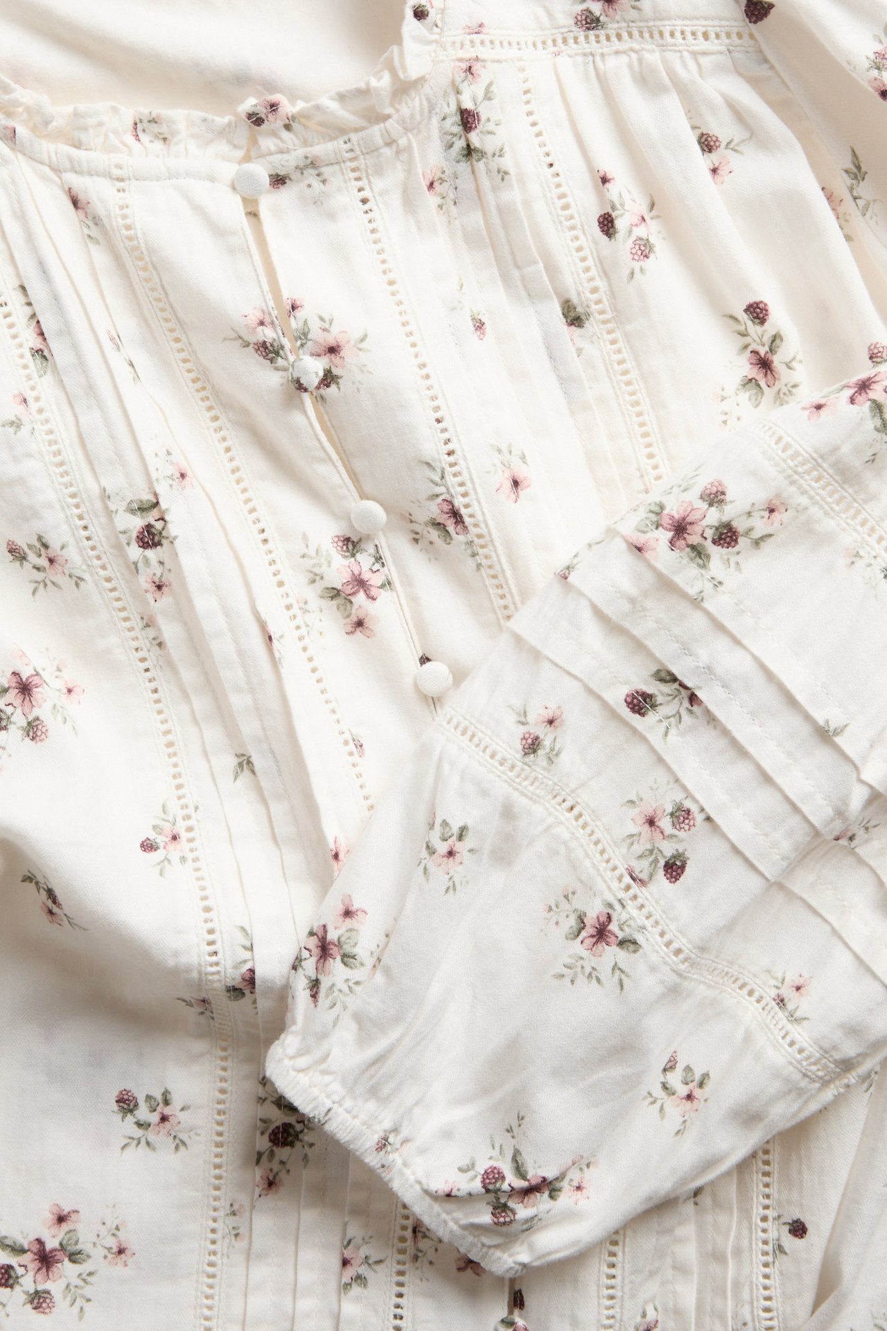 Nahaufnahme einer cremefarbenen Bluse mit Blumenmuster, Knöpfen, Biesen und gerafften Ärmeln.