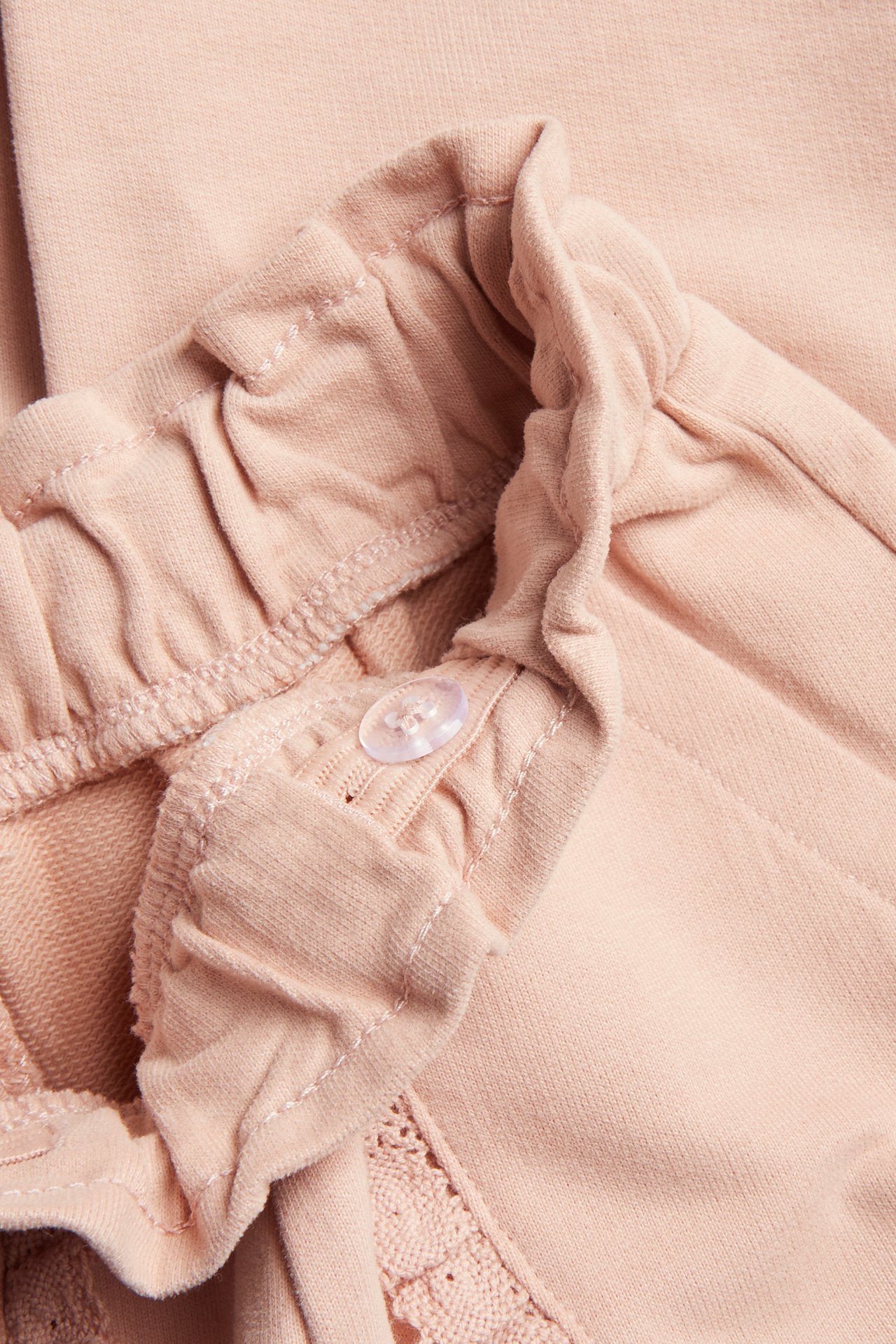 Nahaufnahme einer rosa Baumwoll-Jogginghose mit elastischem Bund, verstellbarem Knopf und Spitzendetails.