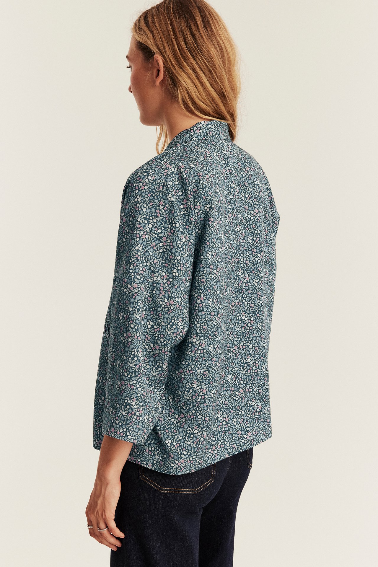 Back view of a woman wearing a teal floral long-sleeve shirt and dark blue jeans.