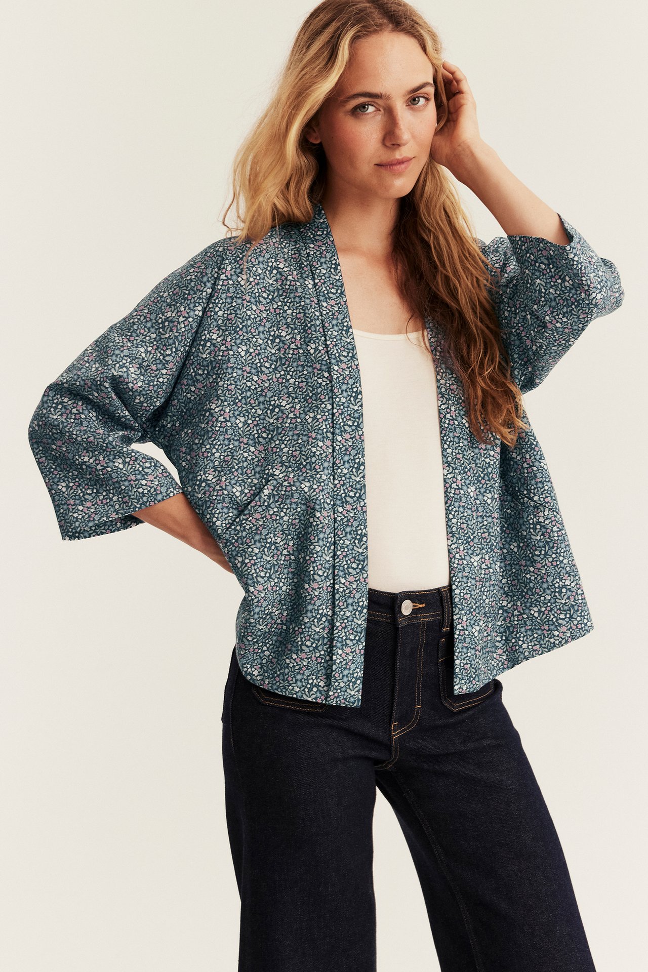 Vorderansicht einer Frau in lockerem blaugrünen Blumen-Kimono über weißem Top und dunklen Jeans.