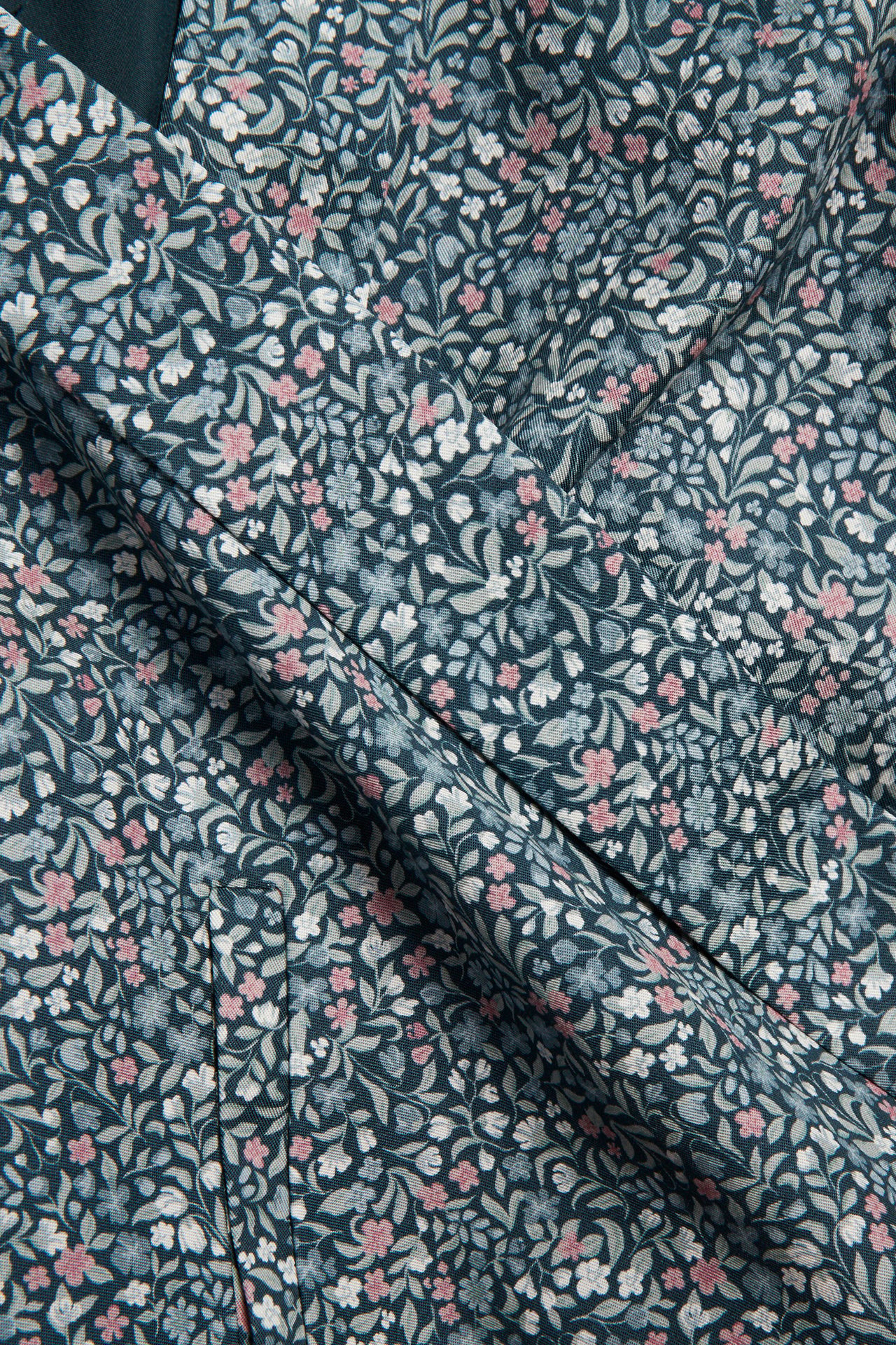 Nahaufnahme eines dunkelpetrolfarbenen Blumenstoffs mit rosa, weißen und hellblauen Blüten und grünen Blättern.