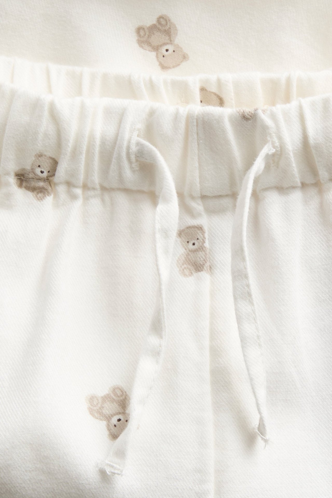 Close-up of off-white cotton woven trousers with a teddy bear pattern and elastic drawstring waist.