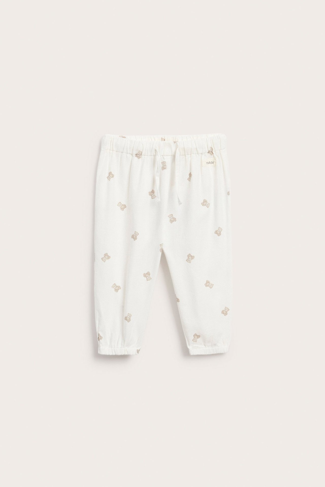 Front view of offwhite woven baby trousers with a teddy bear pattern, elastic waist, and leg cuffs.