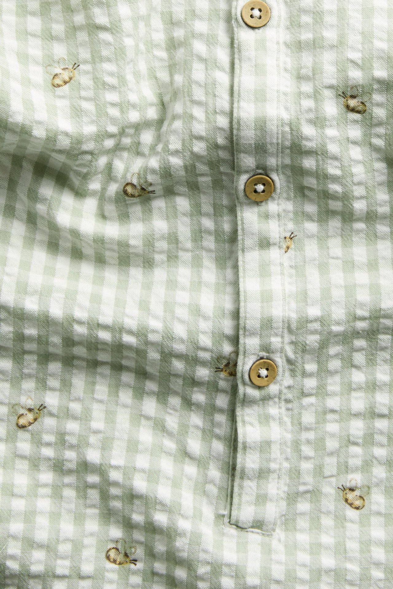 Close-up front view of a green and white checkered cotton romper with embroidered bees and front buttons.