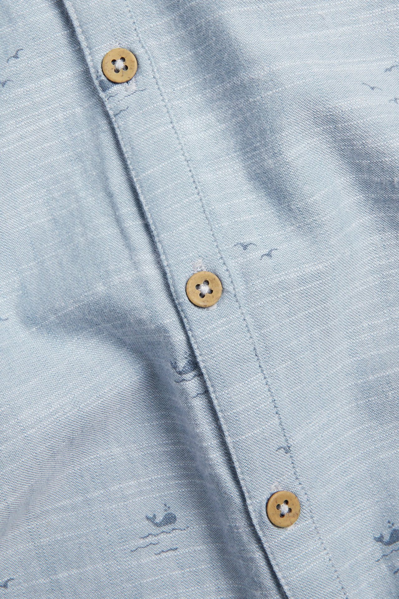 Close-up of a light blue cotton jumpsuit with a whale pattern and wooden buttons.