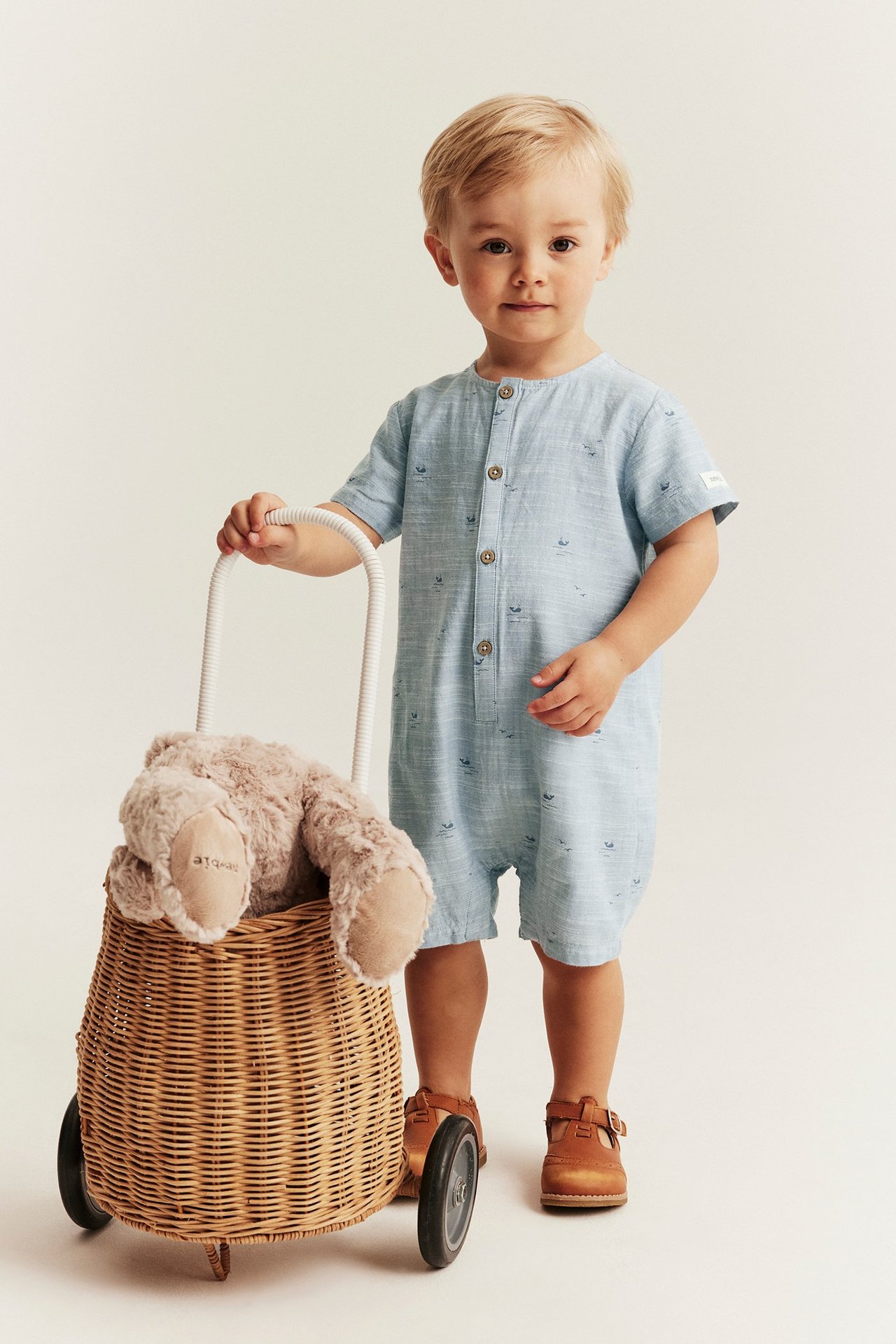 Kind in hellblauem Walmuster-Strampler mit Knöpfen und braunen Schuhen, Vorderansicht.