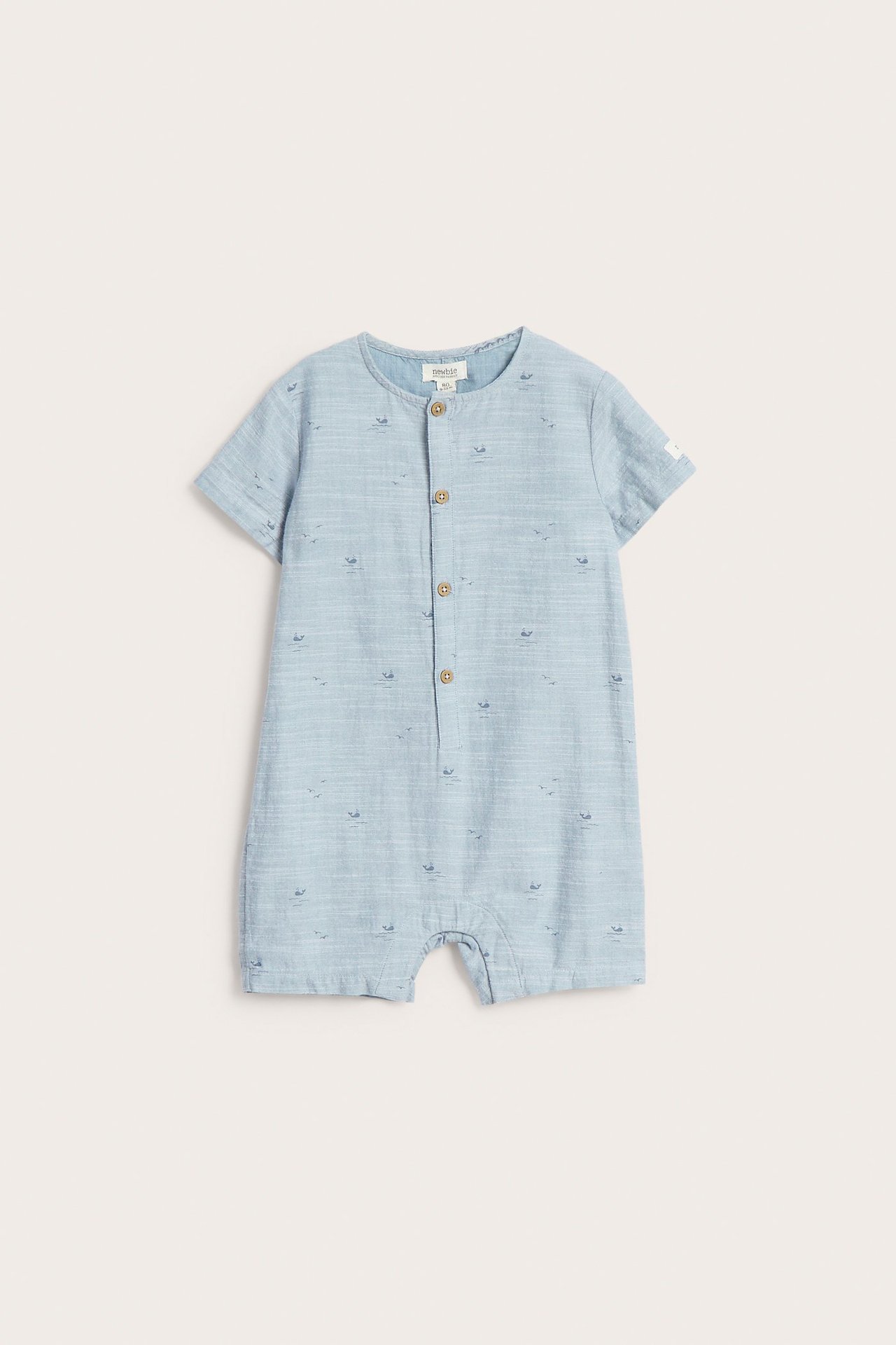 Front view of a blue woven cotton baby romper with a small whale pattern and front buttons.