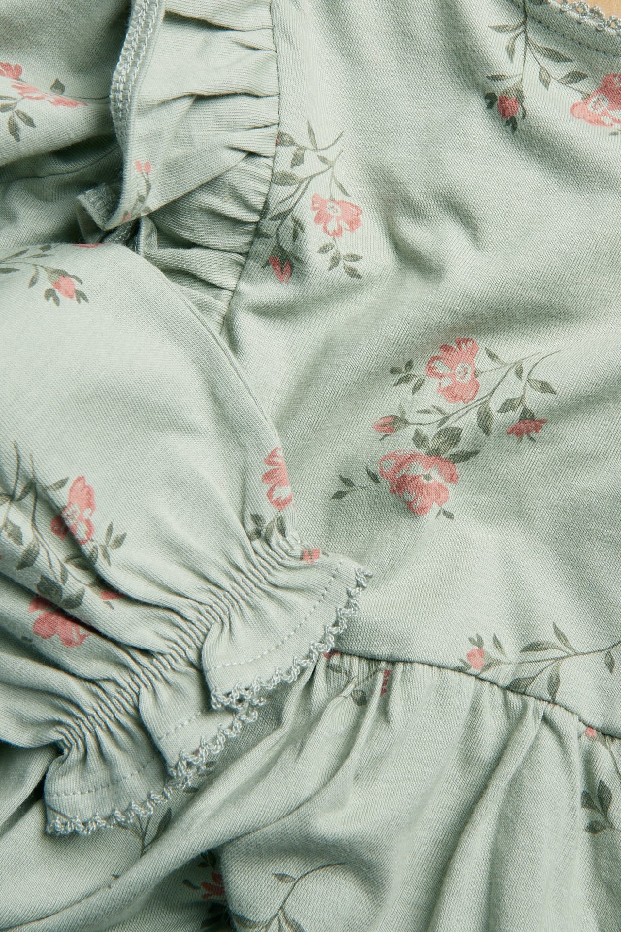 Close-up of a light green floral jersey dress with ruffles, elasticated cuffs, and picot trim.