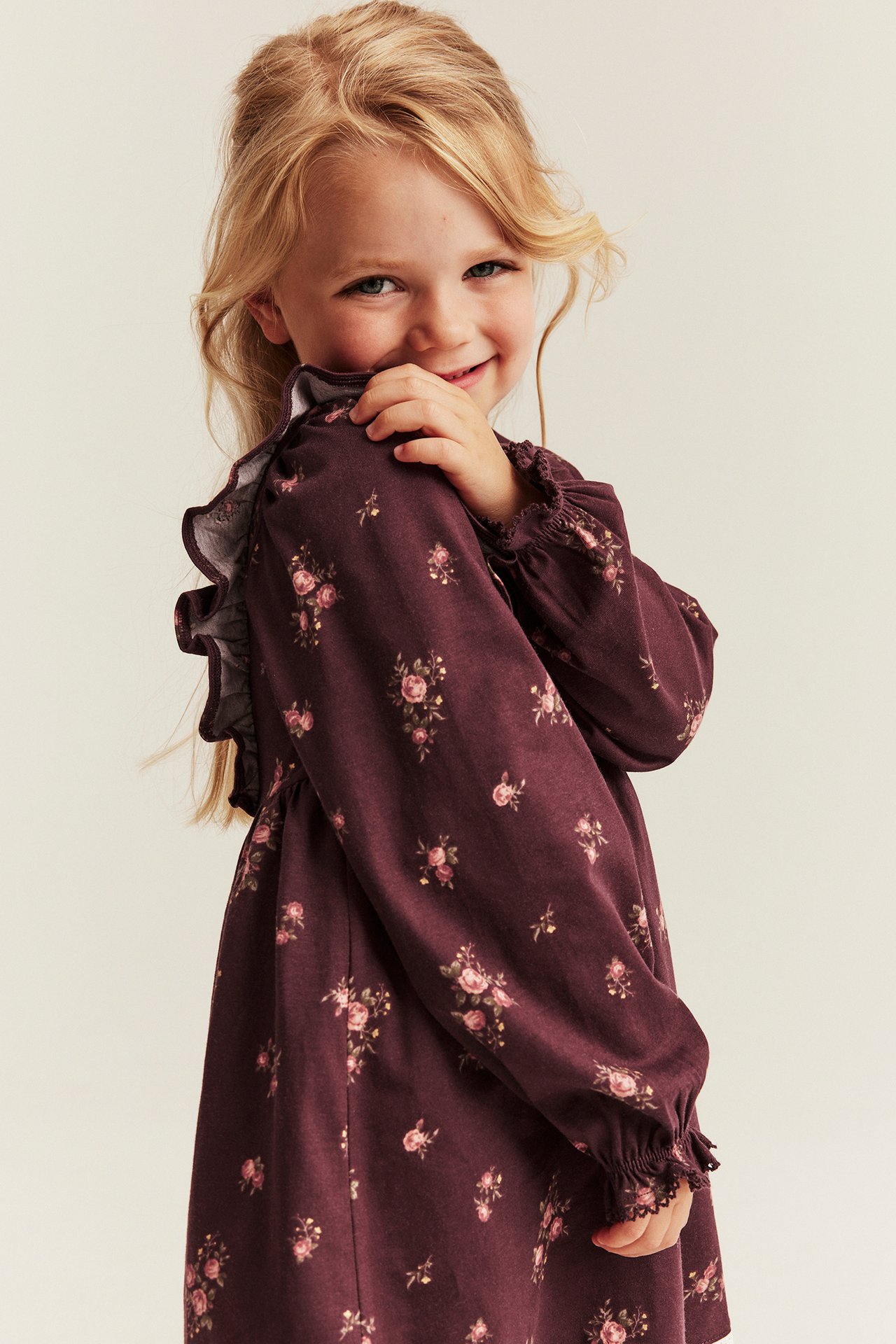 Side view of a kid wearing a dark red floral print long-sleeved dress with ruffles.