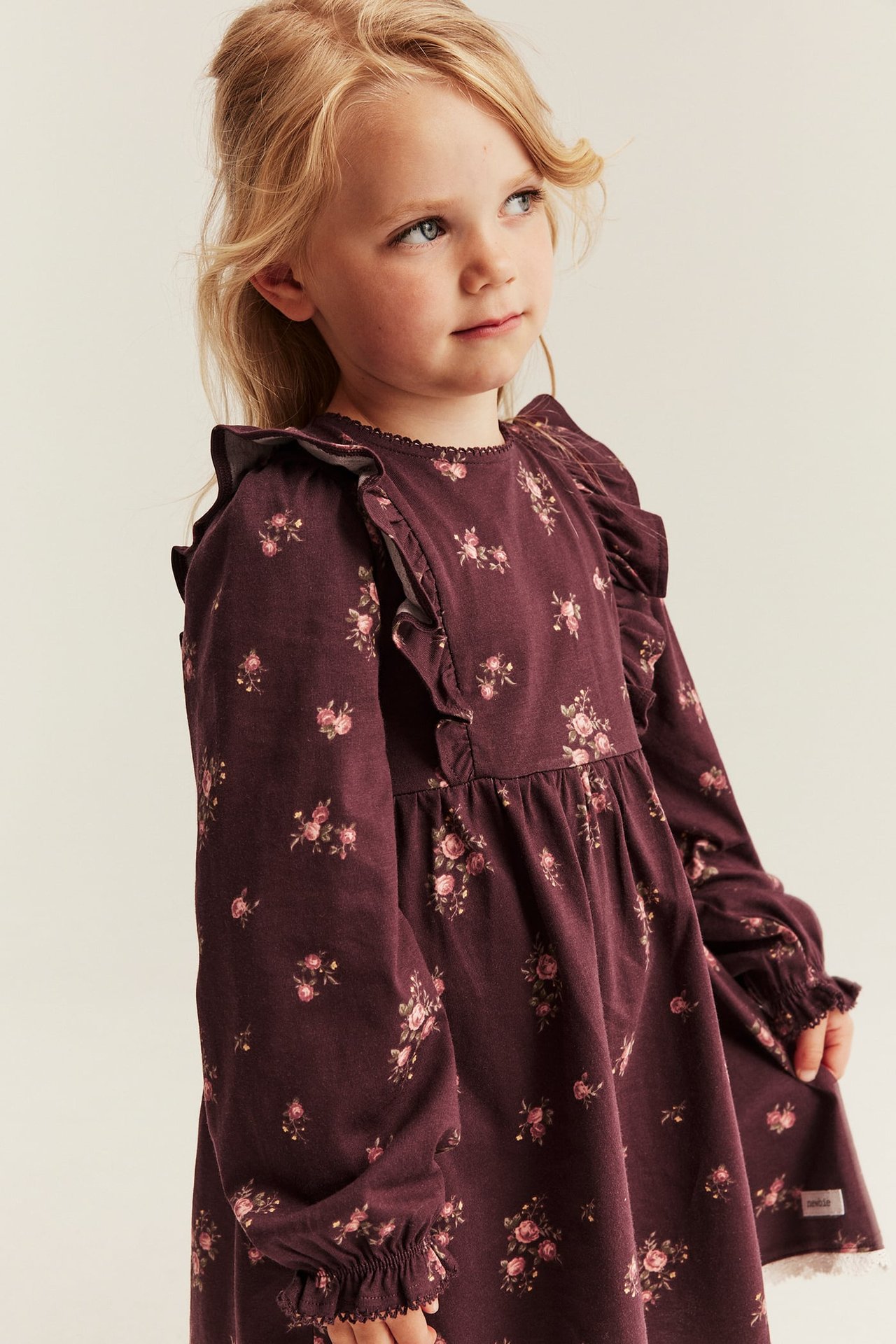Kid's plum floral long-sleeved dress with ruffles, front-side view.