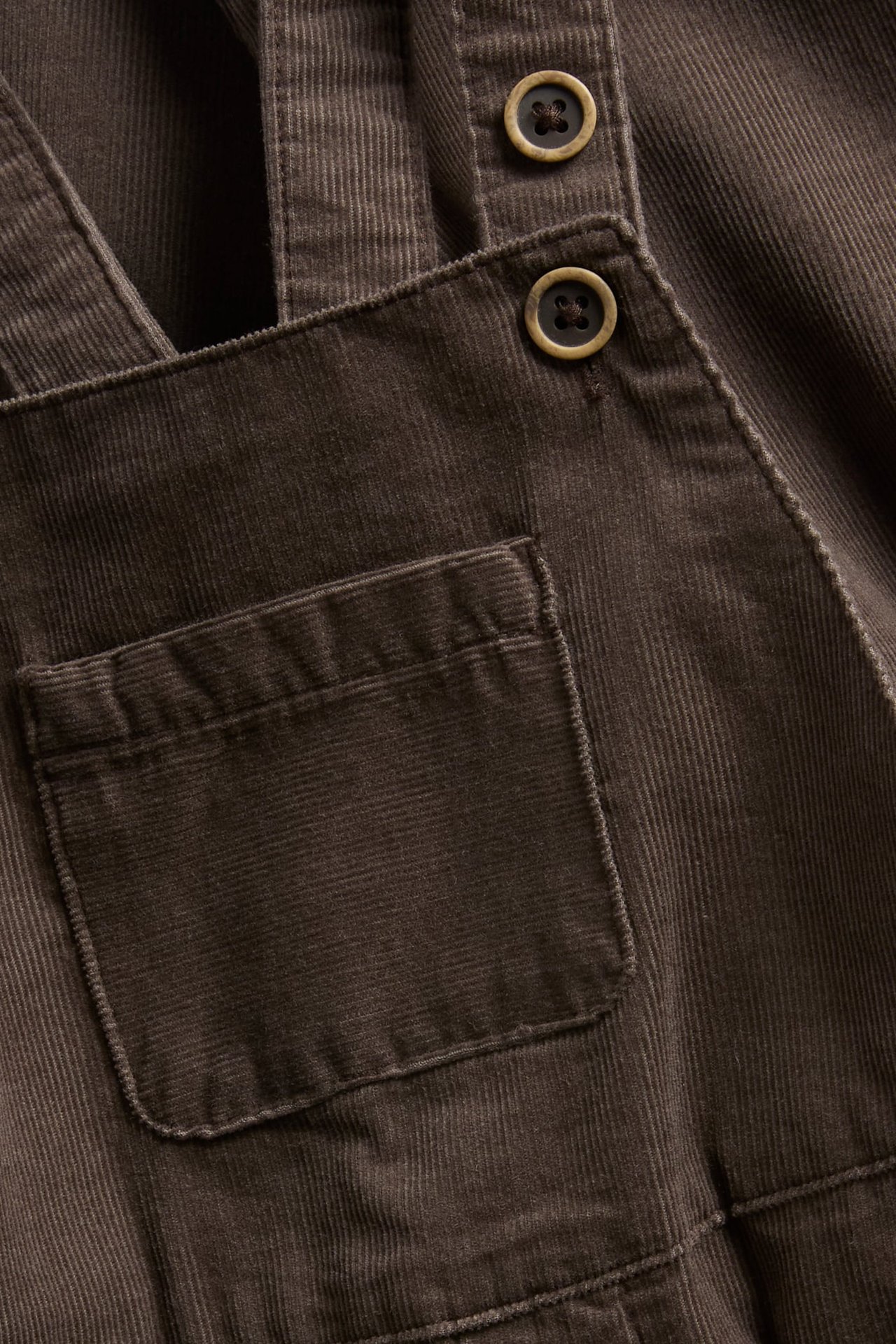 Nahaufnahme einer dunkelbraunen Cord-Latzhose mit Knöpfen und einer aufgesetzten Tasche.