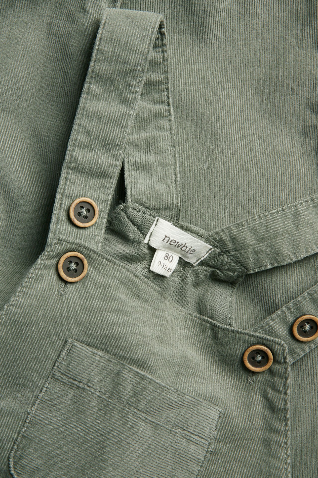Close-up of green baby corduroy overalls with wooden buttons.
