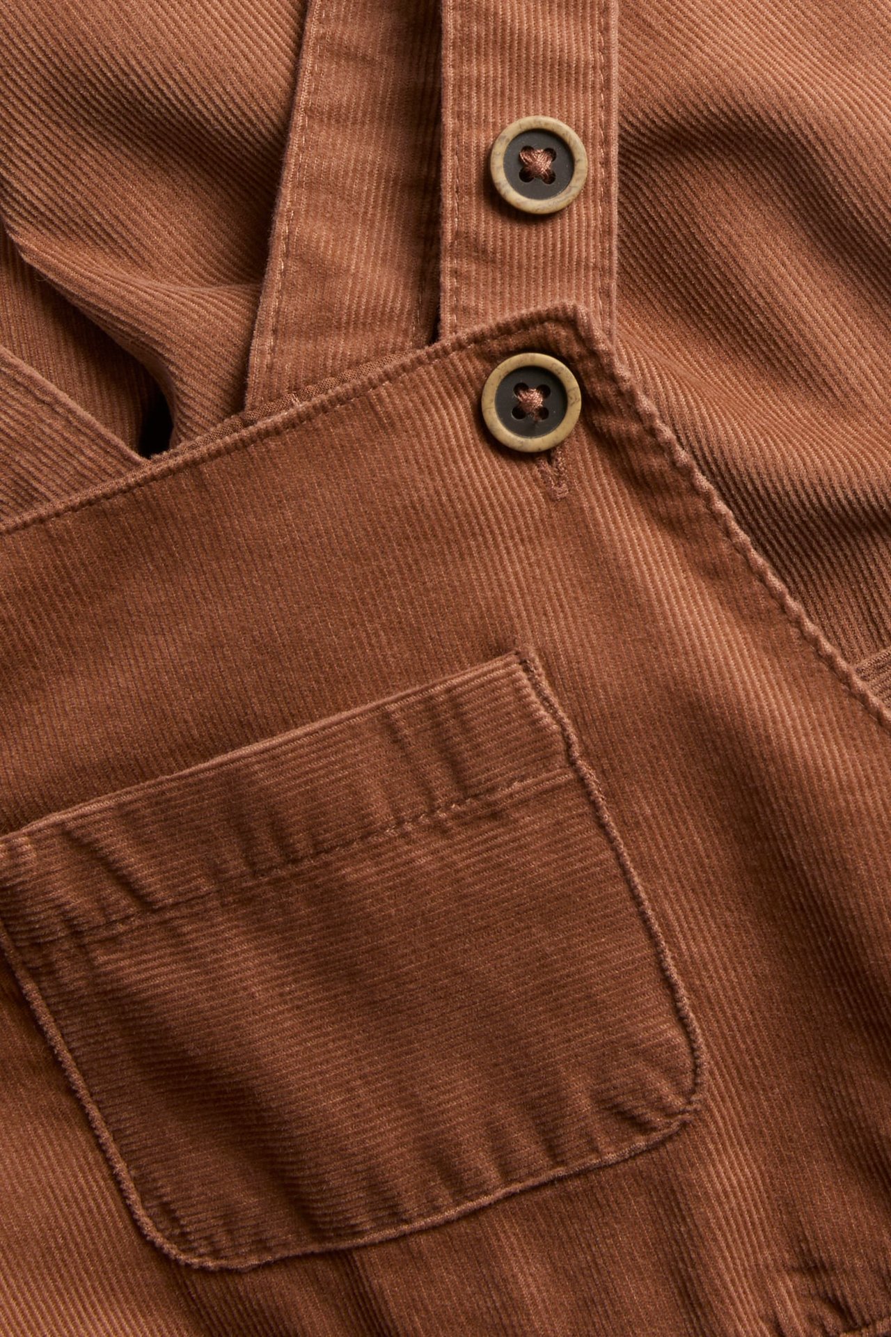 Nahaufnahme von braunen Cord-Overalls mit Knöpfen und einer Vordertasche.