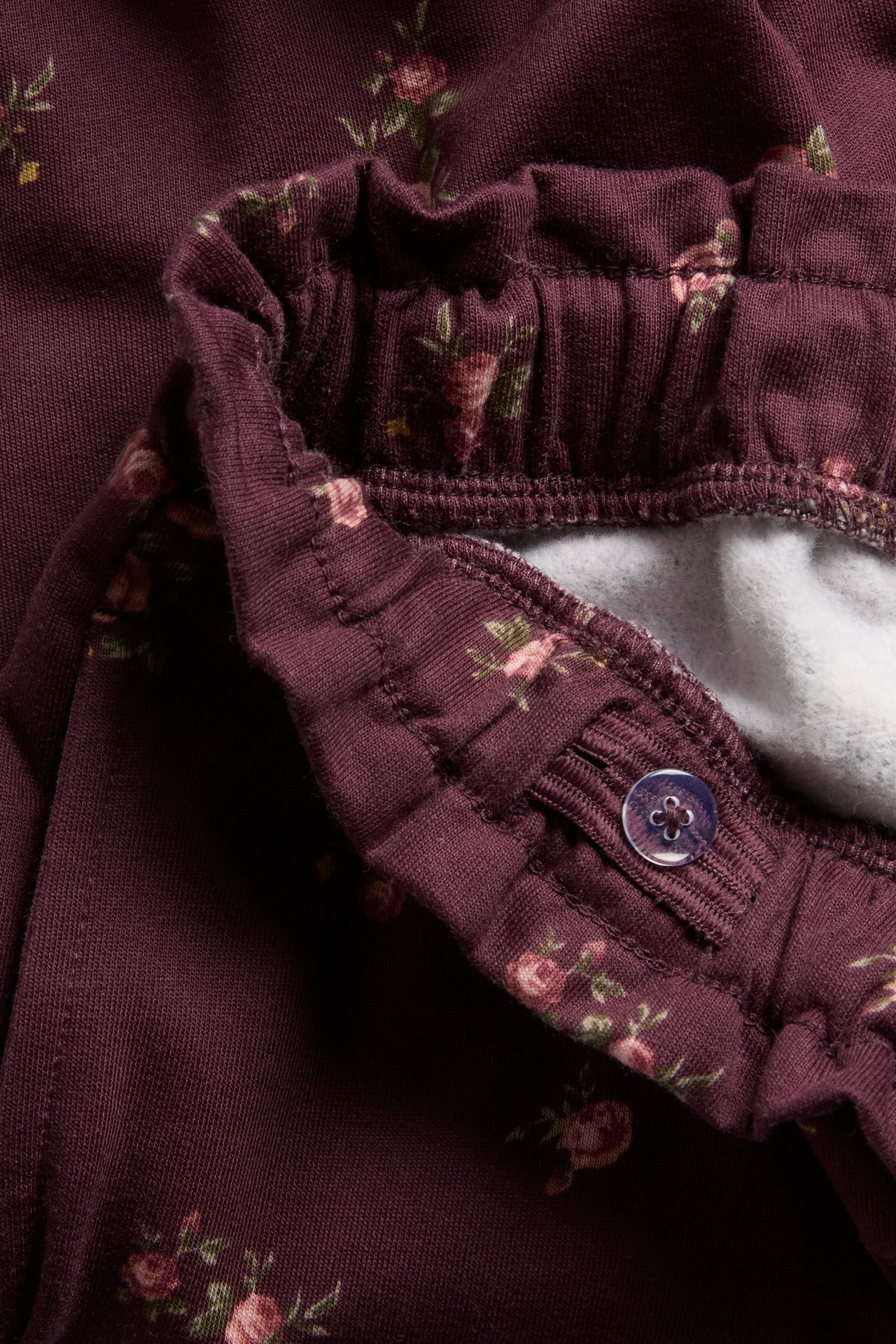 Close-up of kid's dark red floral print pants with an adjustable elastic waist and purple button.