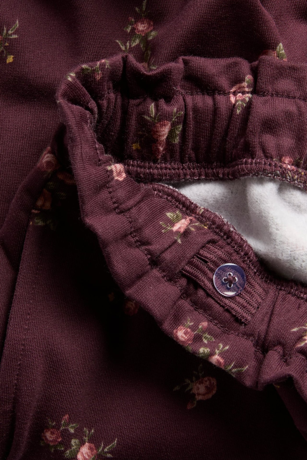 Close-up of kid's dark red floral print pants with an adjustable elastic waist and purple button.