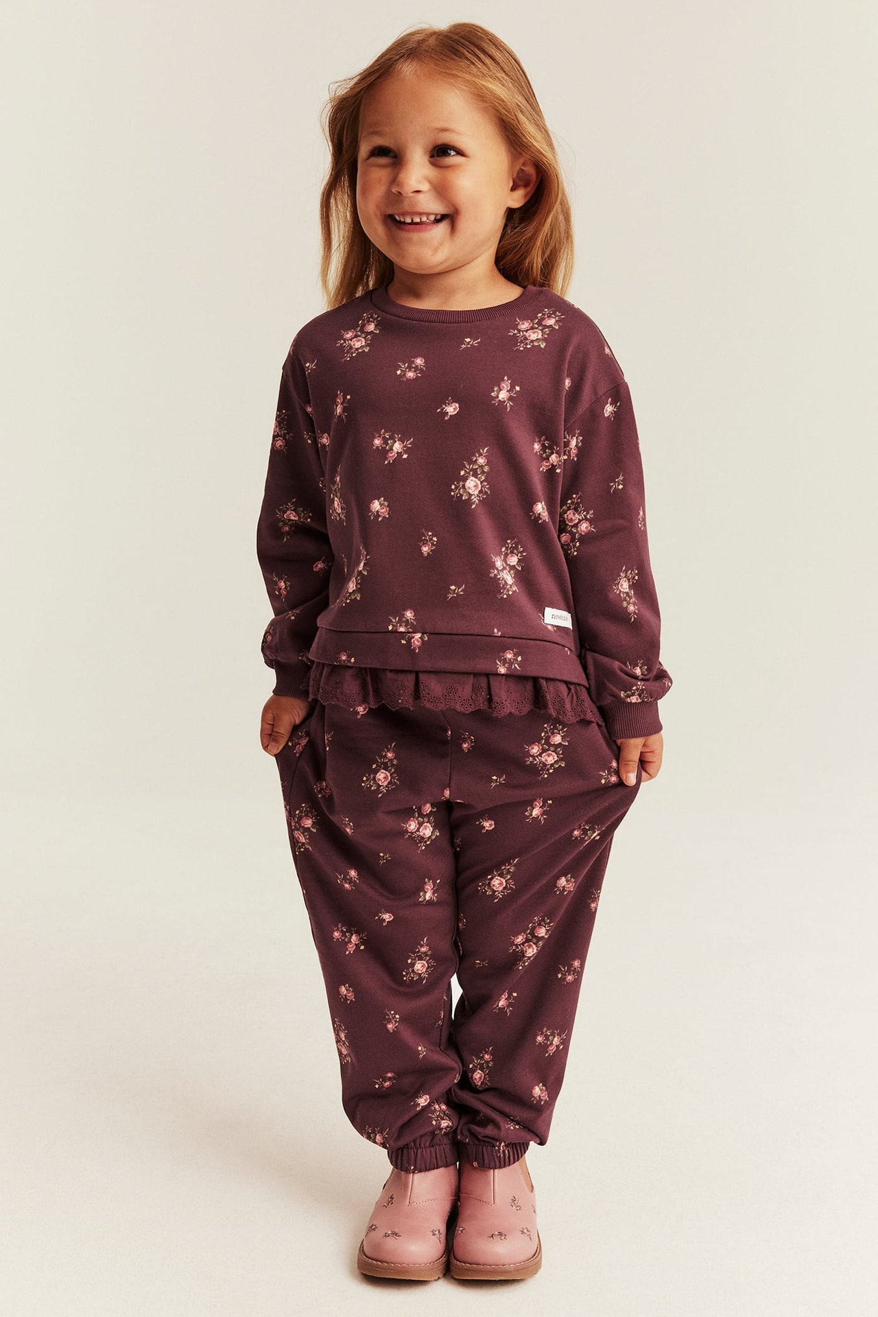 Front view of a kid wearing a plum floral print long-sleeve top and matching sweatpants. Pink boots.