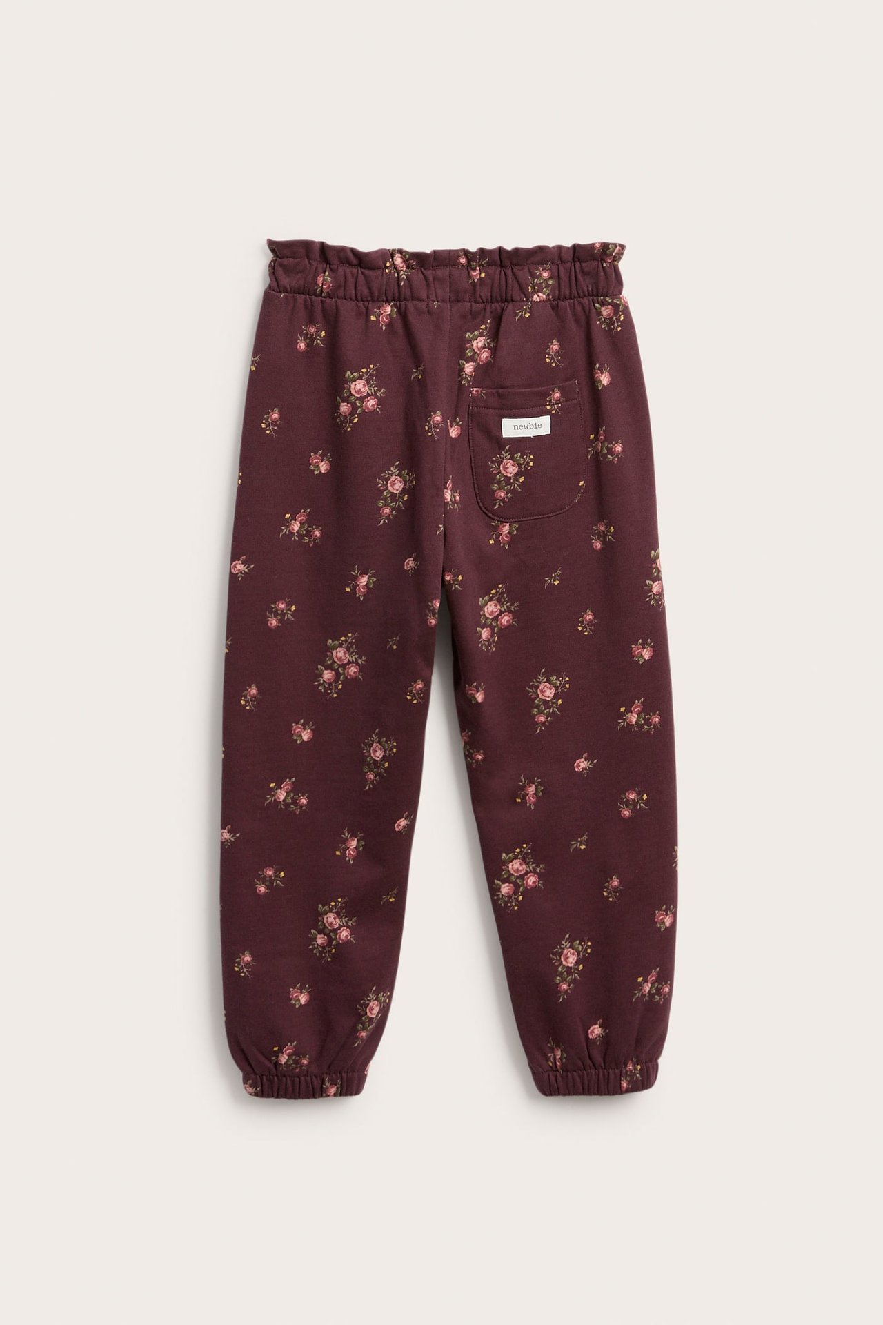 Kid's dark red floral sweatpants, back view, with ruffled waist and elasticated cuffs.