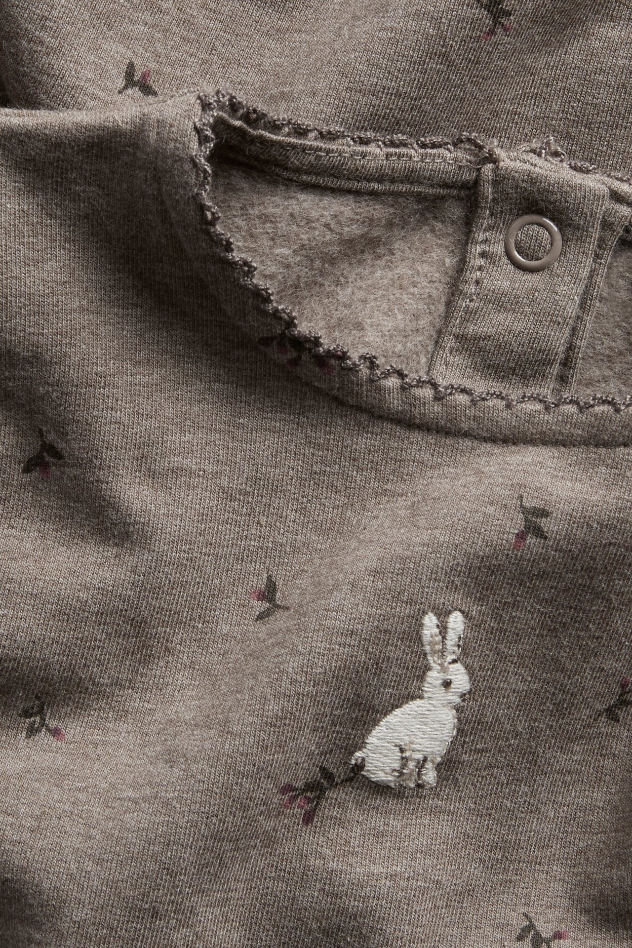 Close-up of a brown baby top with a white bunny embroidery and berry pattern, featuring a snap closure.