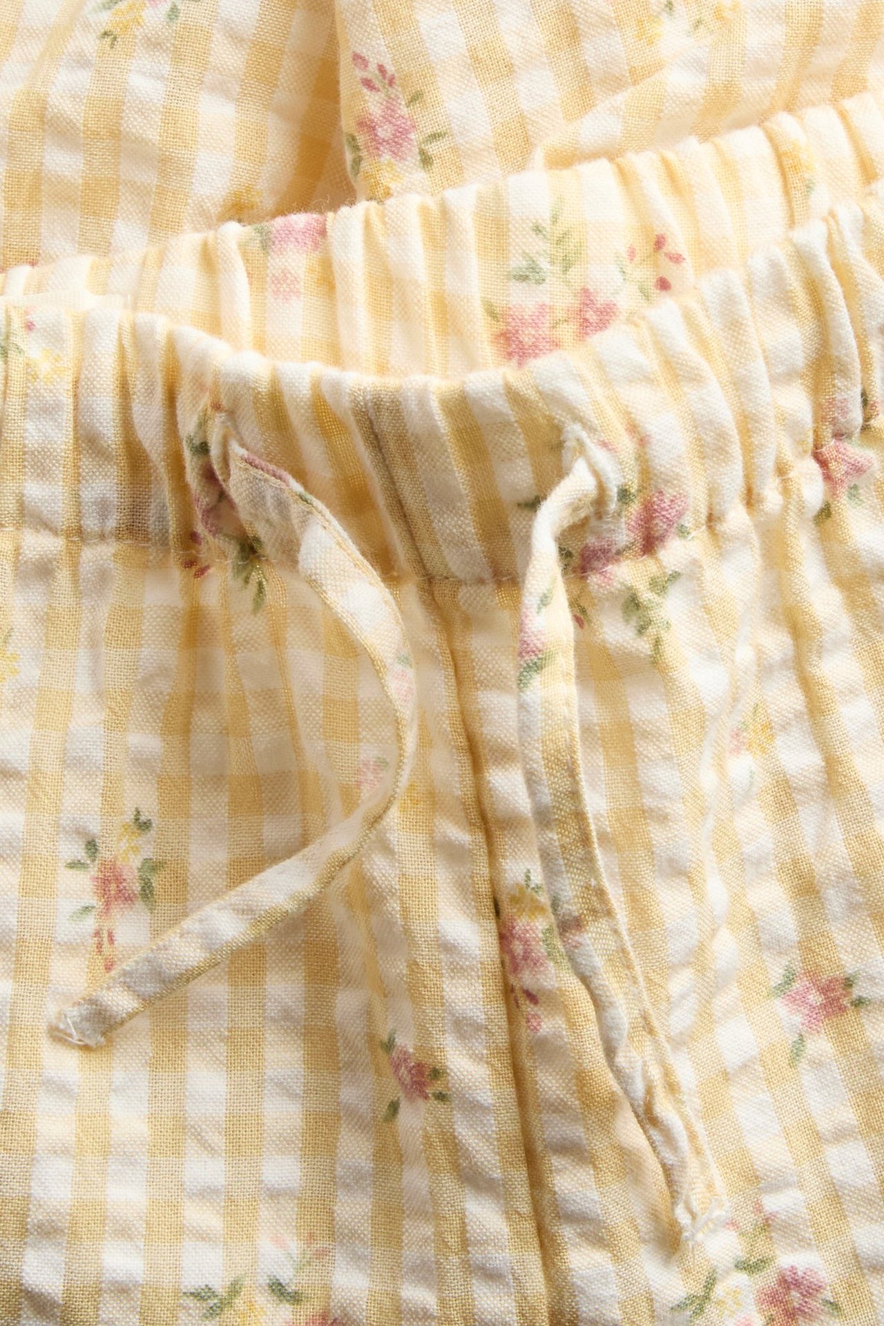 Close-up of yellow and white checkered woven cotton trousers with small floral print and drawstring waist.