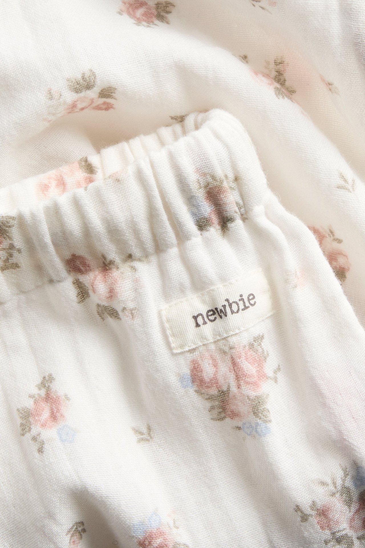 Close-up of off-white thin cotton trousers with a delicate floral pattern and an elastic waistband.