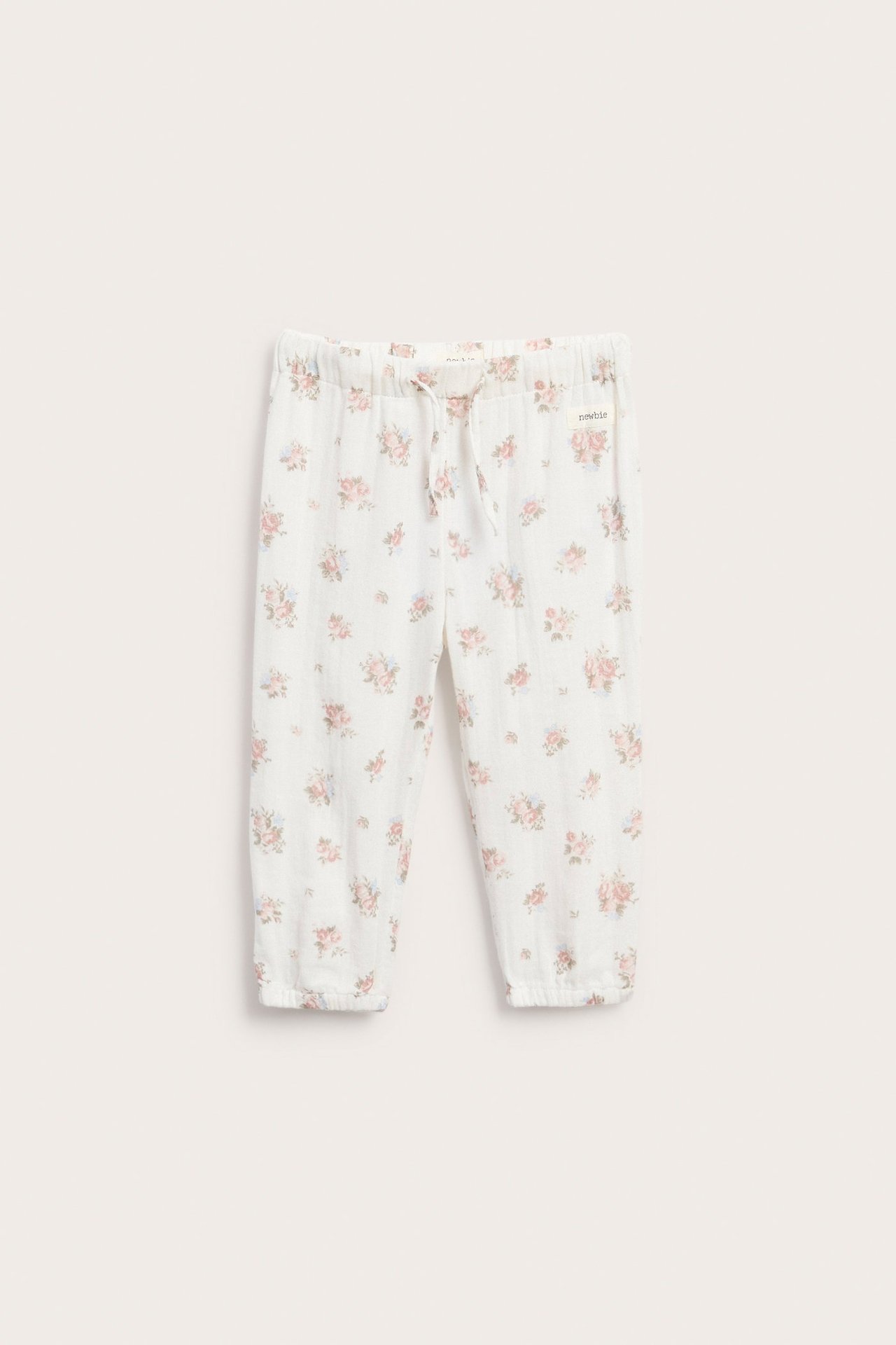 Front view of offwhite woven cotton kid's pants with small pink-blue floral print, elastic waist, and cuffs.