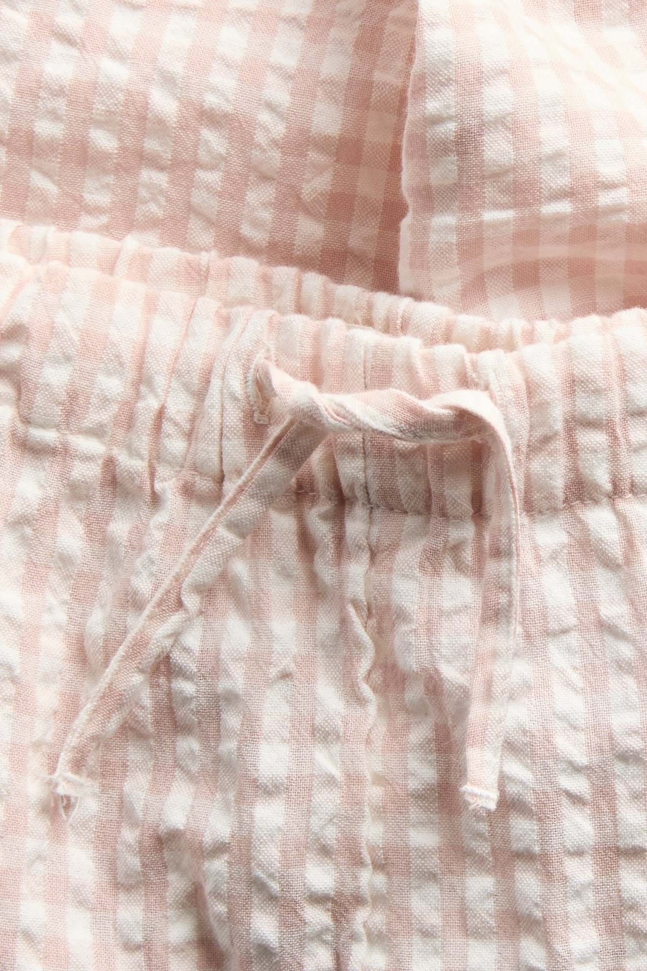 Close-up of light pink checkered cotton woven pants with an elasticated drawstring waist.