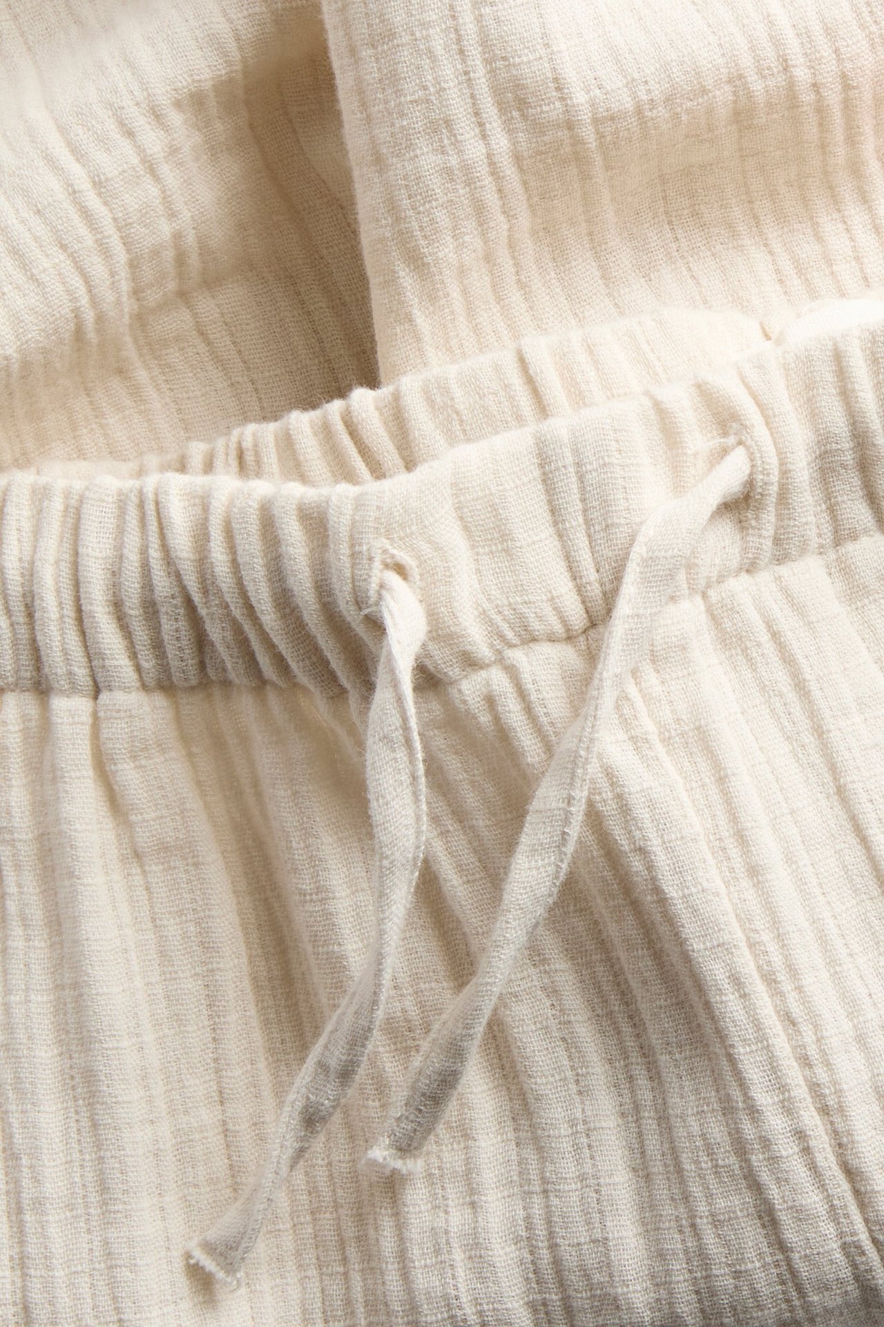 Close-up of light beige woven cotton trousers featuring an elasticated drawstring waist.